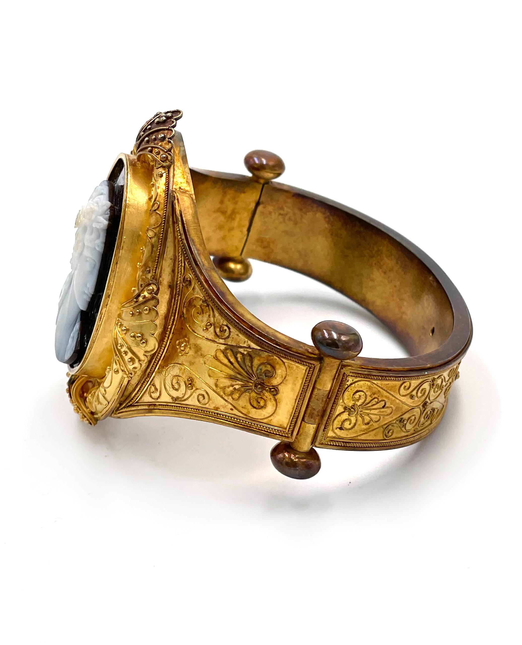 Antique lady's 18K yellow gold hard stone cameo hinged bangle bracelet. The oval cameo measures
33x26mm. The detailed carving depicts a Roman style portrait of a woman.  The stone has a black background and white on the profile. The ornate bracelet