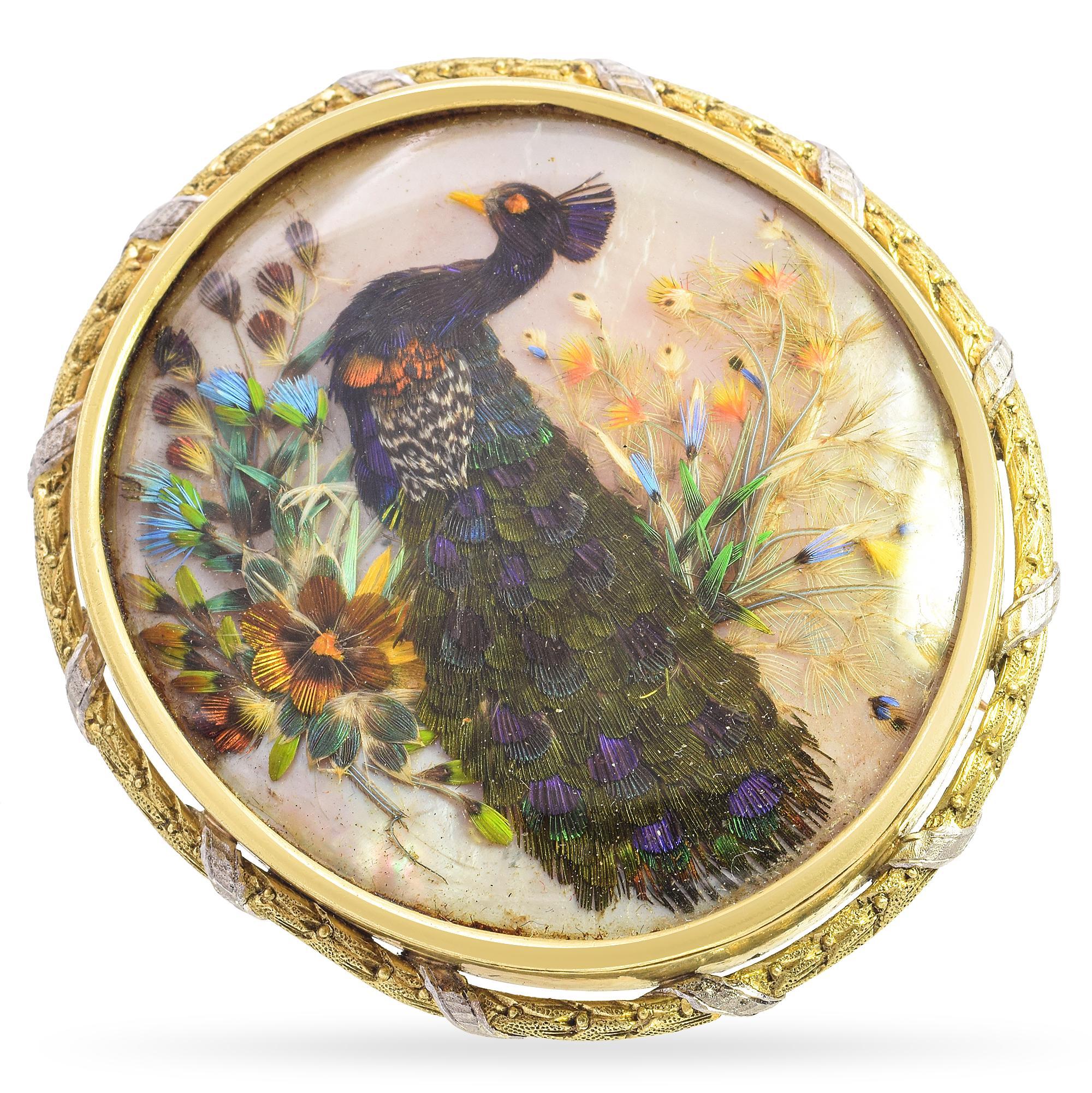 This exquisite antique brooch is a true testament to artistry and craftsmanship. Set in rich 18k gold, it features a luminous mother-of-pearl backdrop that enhances the remarkable peacock feather appliqué. The intricate detailing of the feathers,
