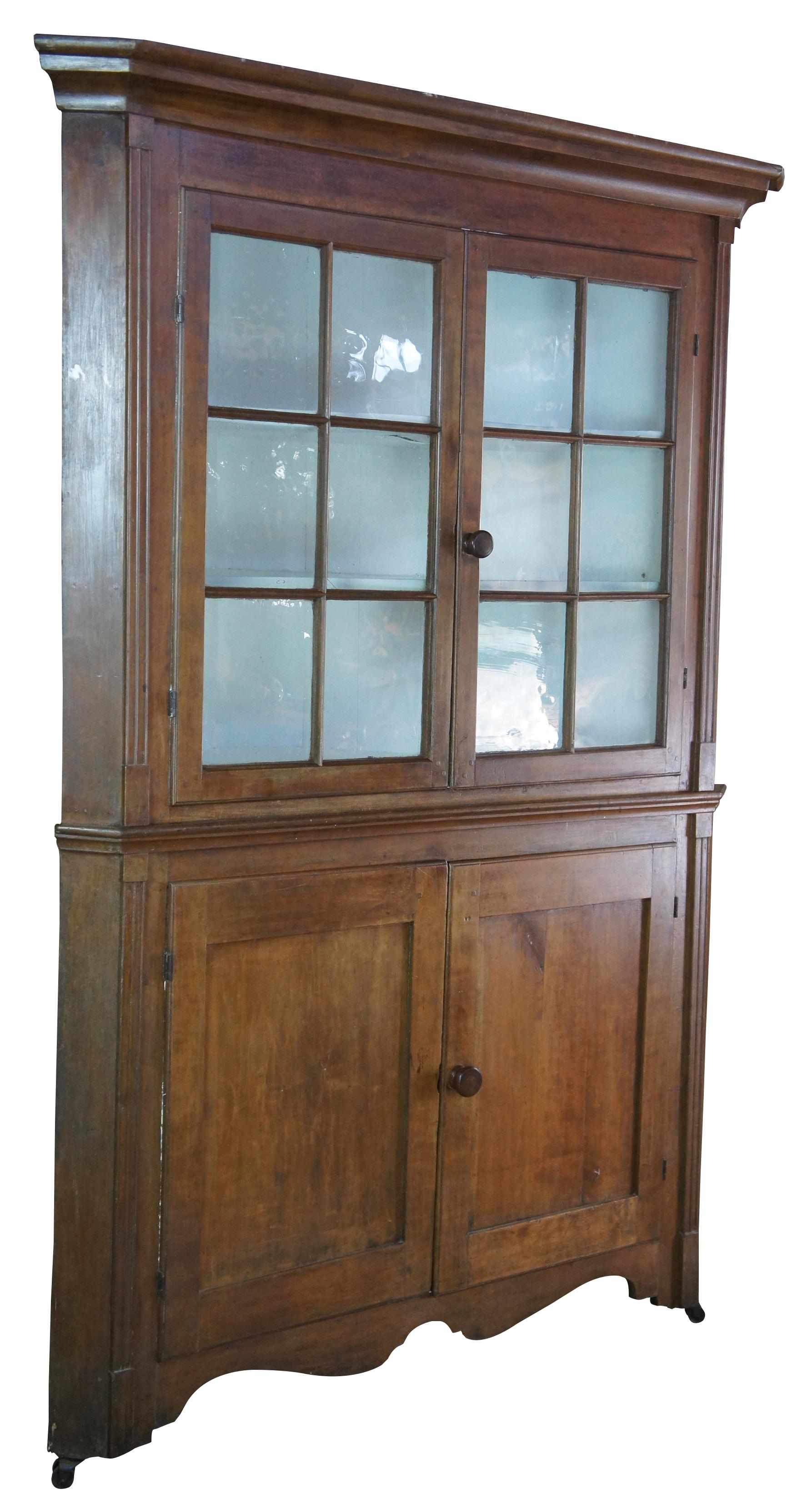 A stately late 18th Century Early American Pennsylvania corner cupboard or cabinet. Made of pine featuring triangular form with serpentine and fluted accents, original glazed wavy glass doors and double casters.
 