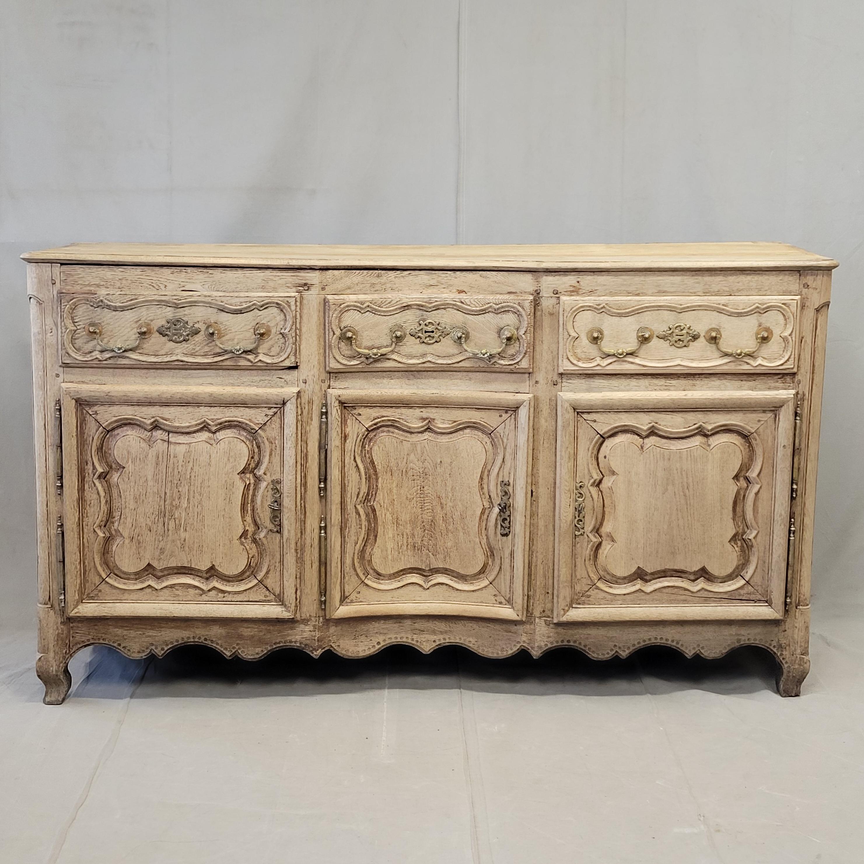 An absolutely stunning antique late 18th century French bleached oak serpentine front sideboard with cast brass hardware. The curving lines of the cabinet front combined with the curvilinear designs around the perimeter of each door and drawer give