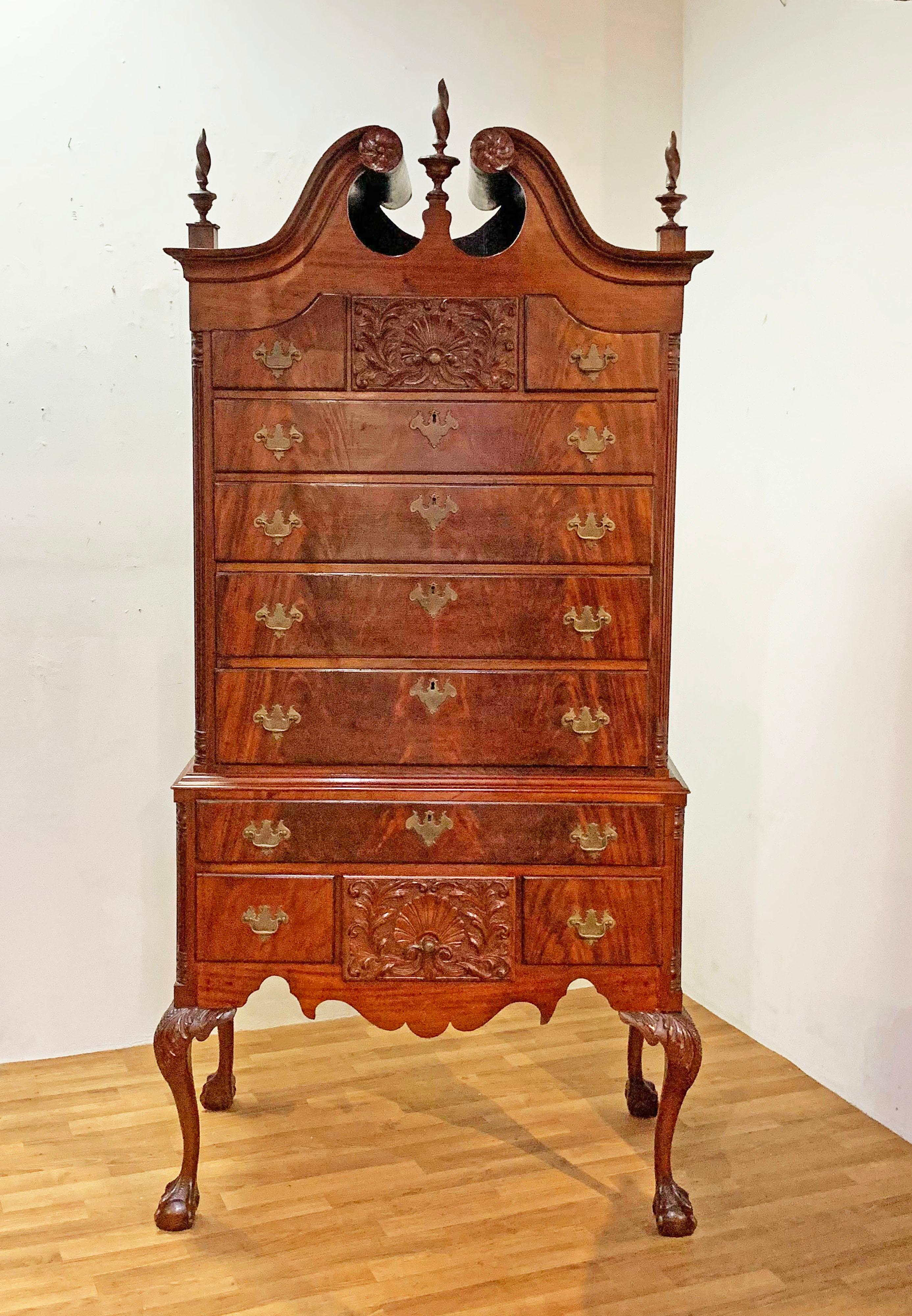 American Chippendale chest on frame highboy dresser in cherry with mahogany drawer fronts. Features a scrolled bonnet with original torch finials, extensively carved shell drawers (both in the upper and lower cases) and is flanked by slender fluted
