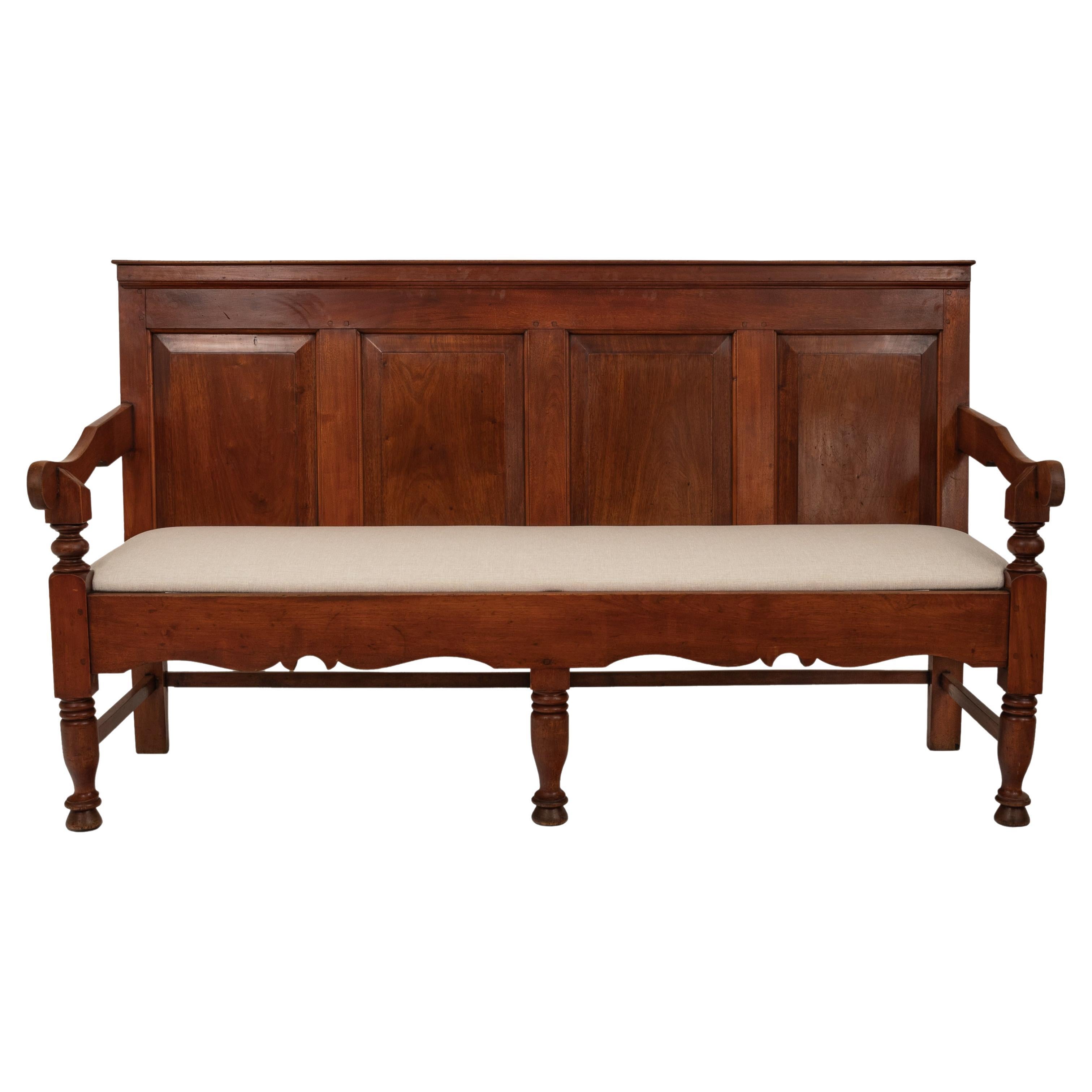 A very good antique American Colonial paneled cherry tavern settle/bench, Circa 1780.
The bench most likely from New England having four fielded panels to the back and a curved armrest at each side, each raised on turned supports. The drop in seat