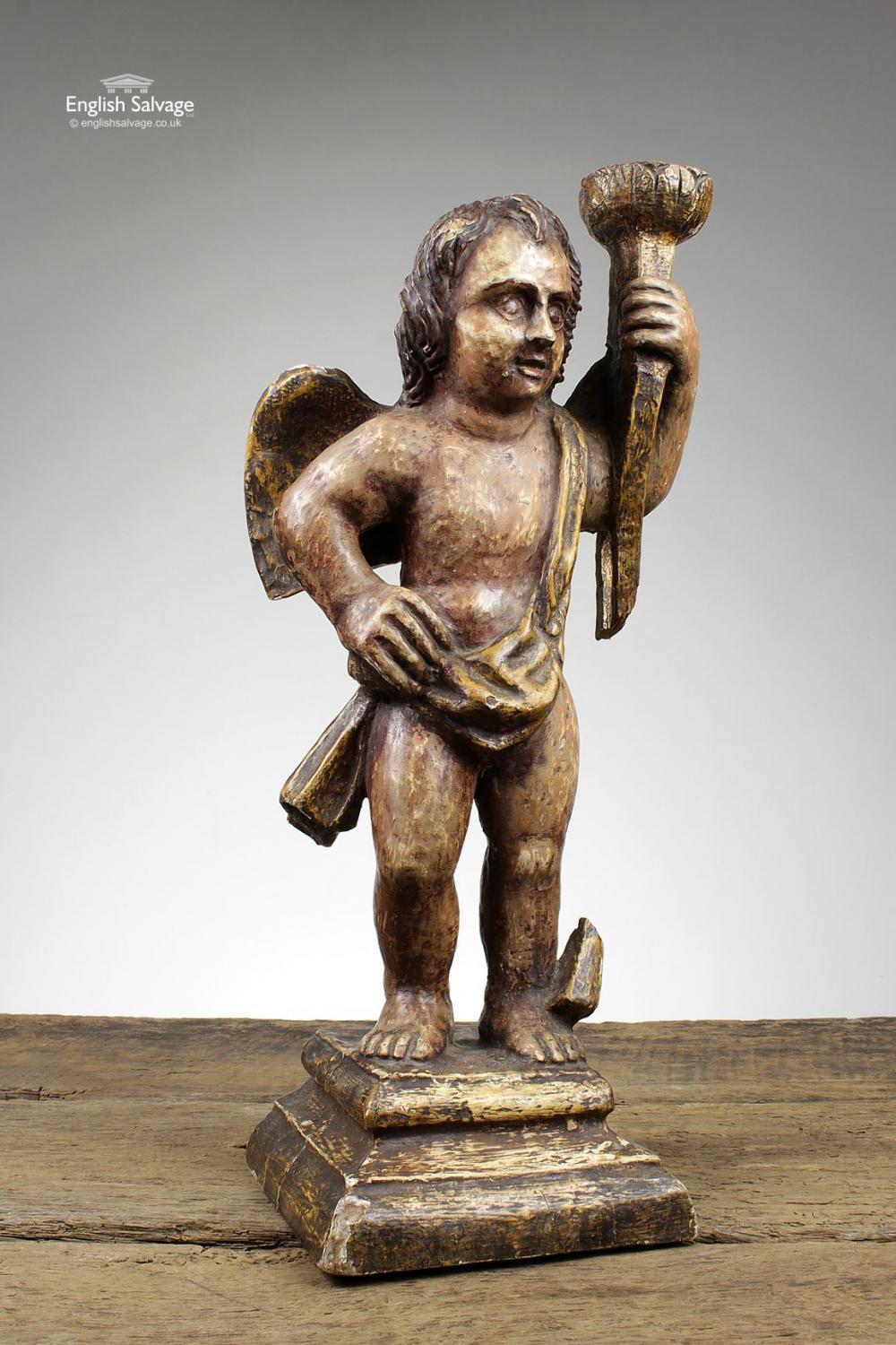 Reclaimed 18th century (or possibly earlier) hand carved wooden statue depicting a cherub holding a torch. The torch may have originally extended into a floor length torchère as it is broken at the base, as is the support next to the cherub's feet.