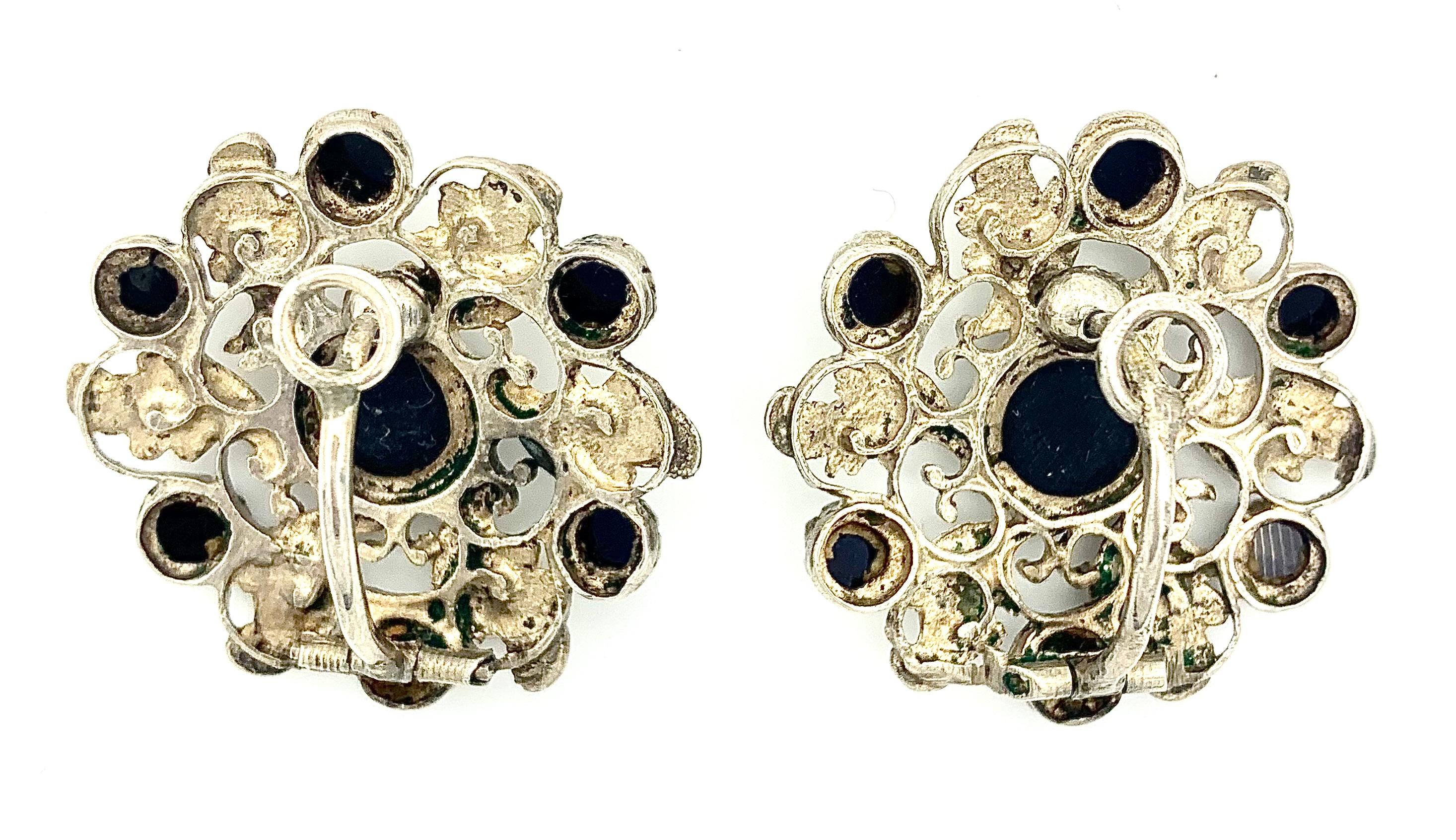 Questa rara e insolita coppia di  gli auricolari a clip in argento sono disegnati come ruote con foglie d'accanto.
I cerchi sono caratterizzati da pietre di vetro nere sfaccettate.
