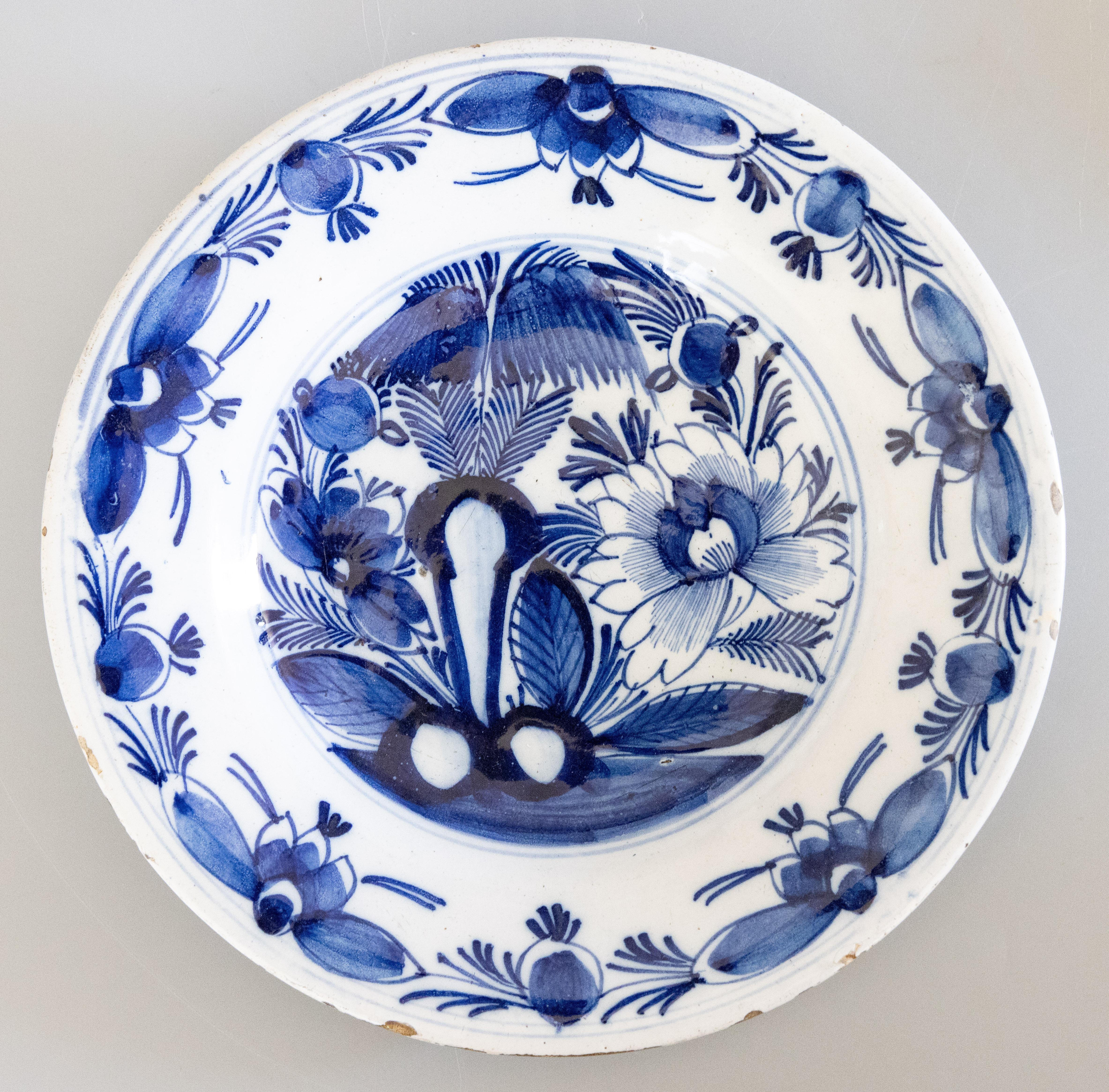 Antique 18th-Century Dutch Delft faience flower plates, featuring an oversized peony, willow tree, and hardscaping. The wide border reveals water lilies and budding flowers.