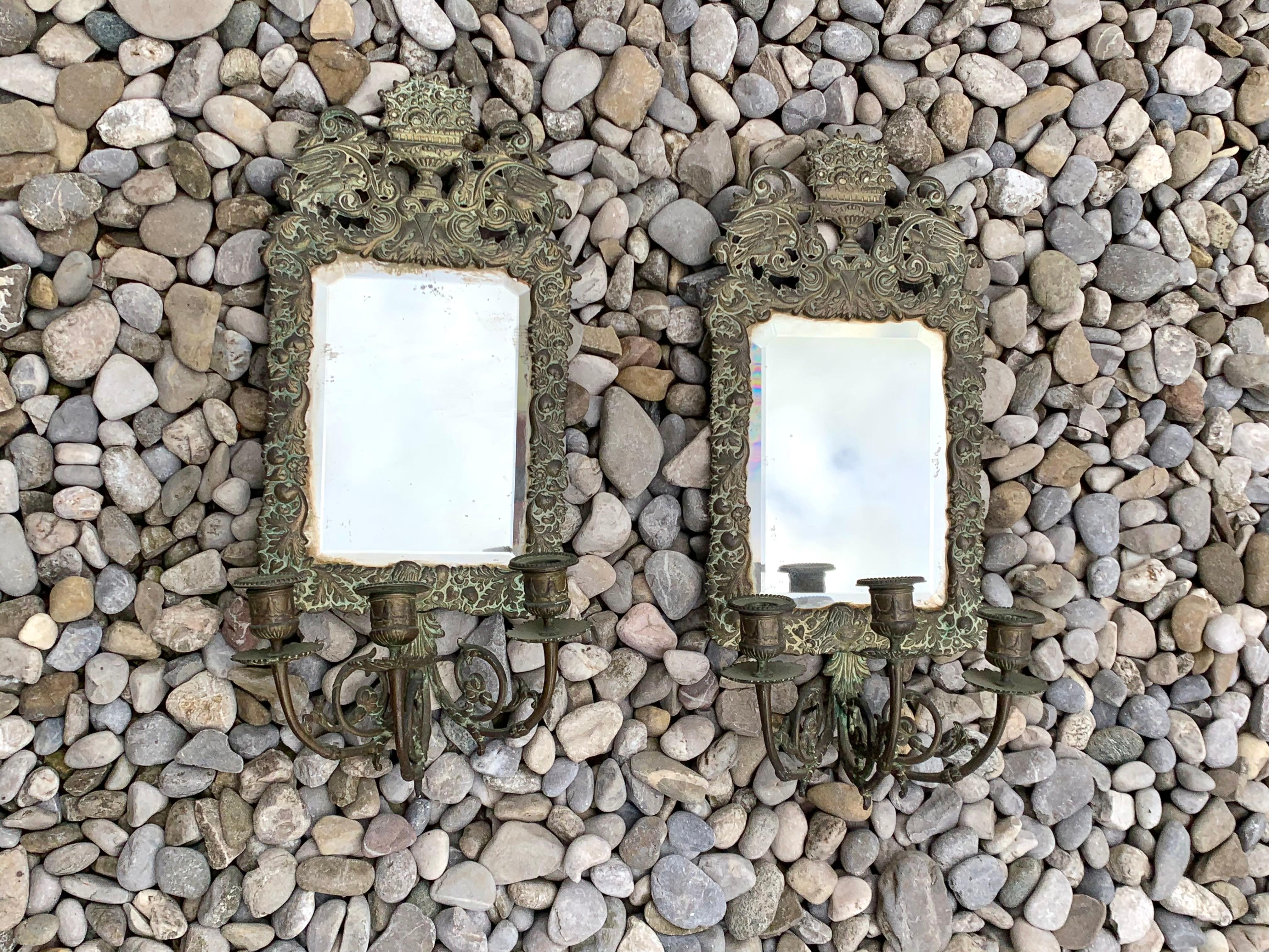 This pair of 18th centurty repoussé brass walls sconces has retained it's original condition and patina as well as the original mirror glass. A pair of eagles surround a basket full of flowers. The mirrors are surrounded by fruits, leaves and