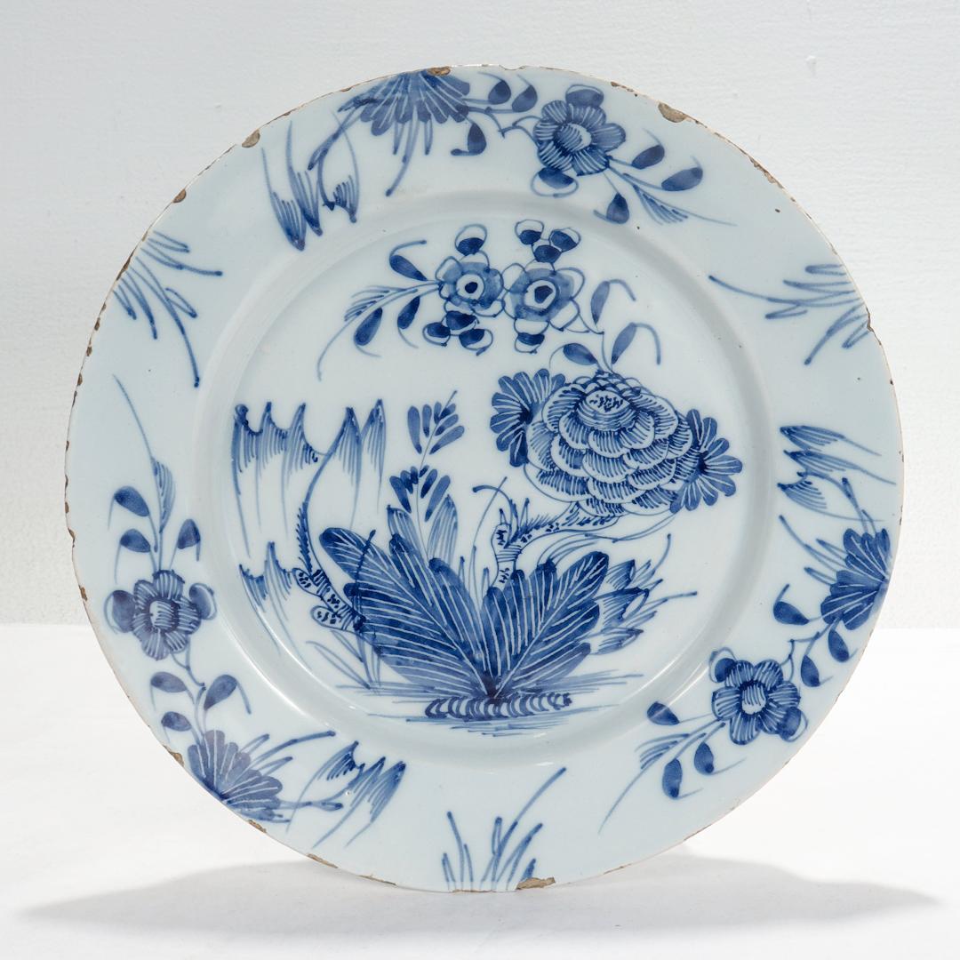 A fine antique 18th century Dutch Delft plate.

Depicting a large peony surrounded by a variety of other flora. Framed by a border with blue decorated flowers and grasses.

Simply a wonderful antique Chinoiserie decorated Delft plate!