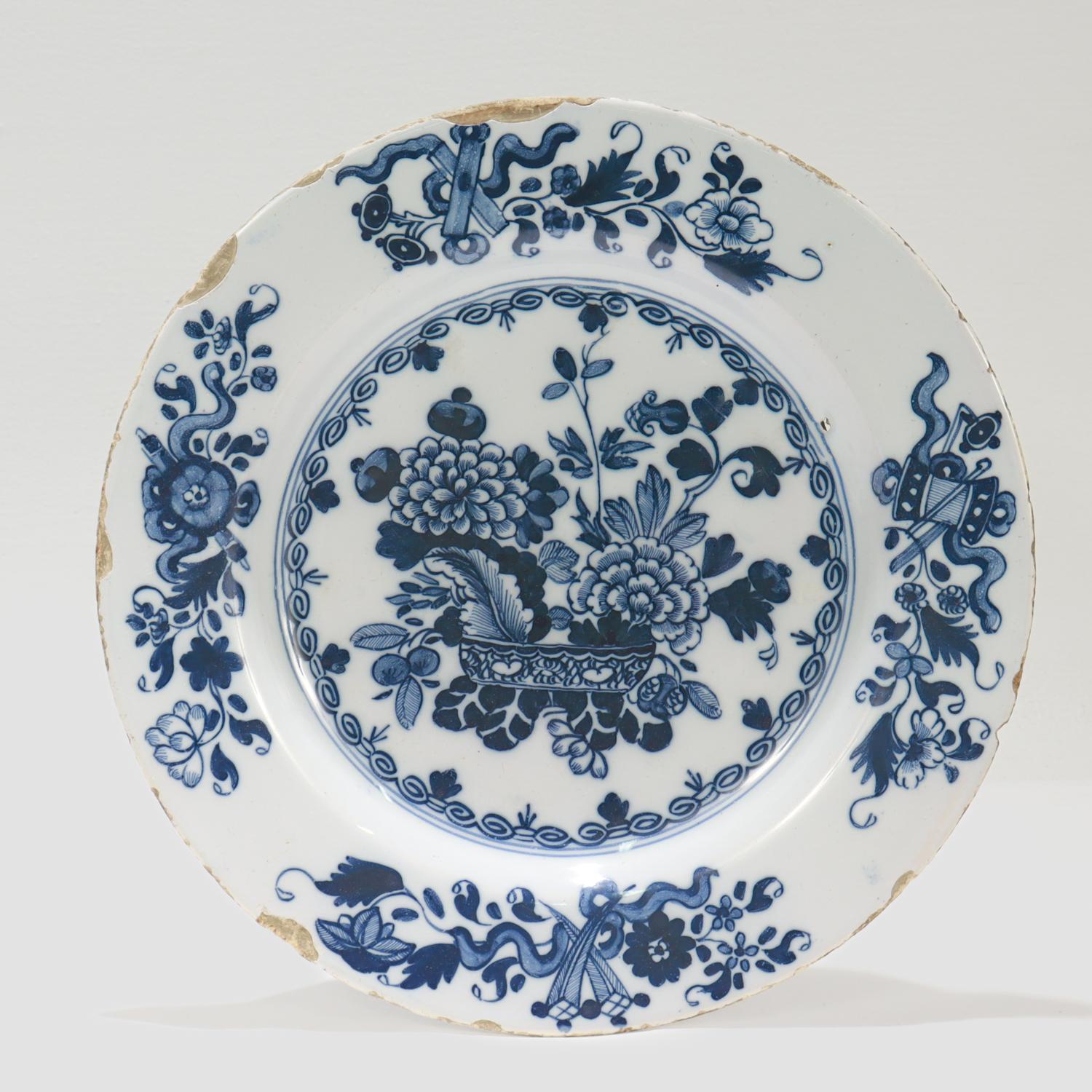 Une belle assiette anglaise ancienne de Delft.

Avec un large bord plat et un puits peu profond.

Le puits est décoré d'une corbeille de fleurs comprenant des chrysanthèmes, des frondes de fougères et des feuilles.

Le bord est décoré de gerbes de