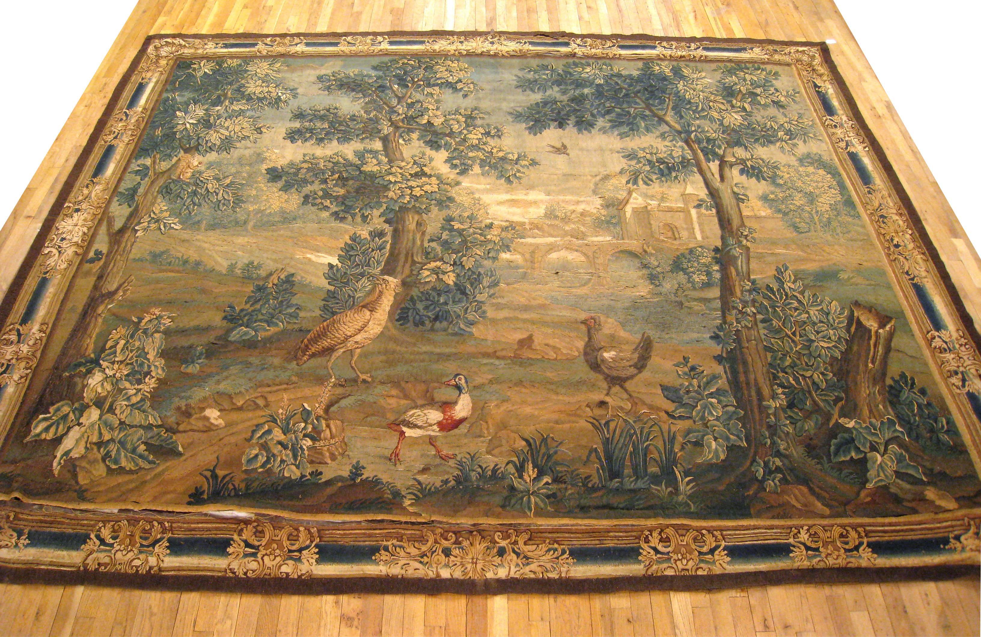An antique 18th century French Beauvais landscape verdure tapestry, size 12'1 H x 10'1 W. This tapestry features a group of birds in a verdant woodland setting near a bridge, with the birds appearing at center between trees, acanthus plants, and