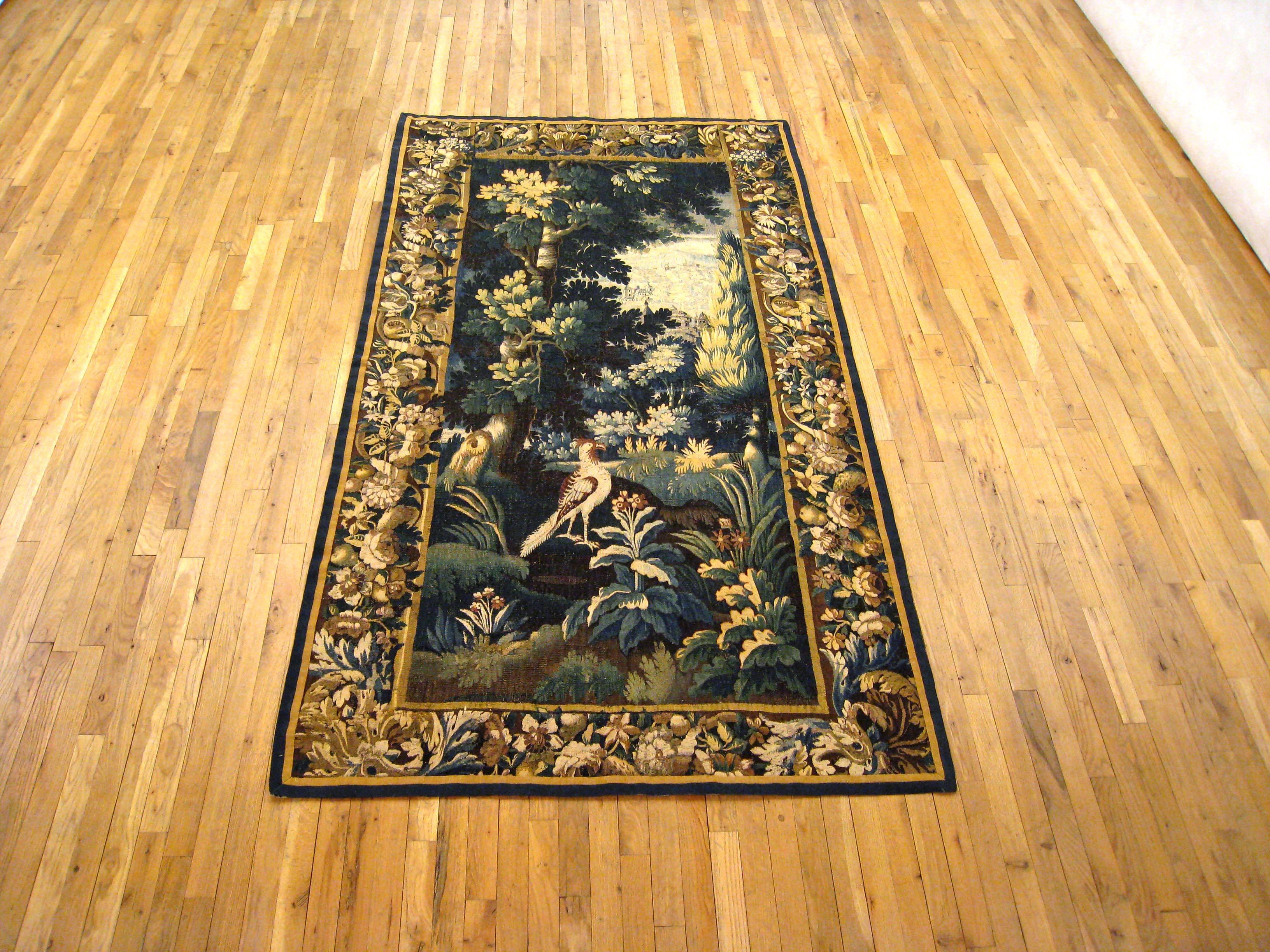 An antique 18th century Flemish verdure landscape tapestry, size: 8.0 H x 4.6 W. This fine handwoven European wall hanging features a lovely landscape scene, with an exotic bird in a lush verdant setting. Enclosed within an elaborate scrolling