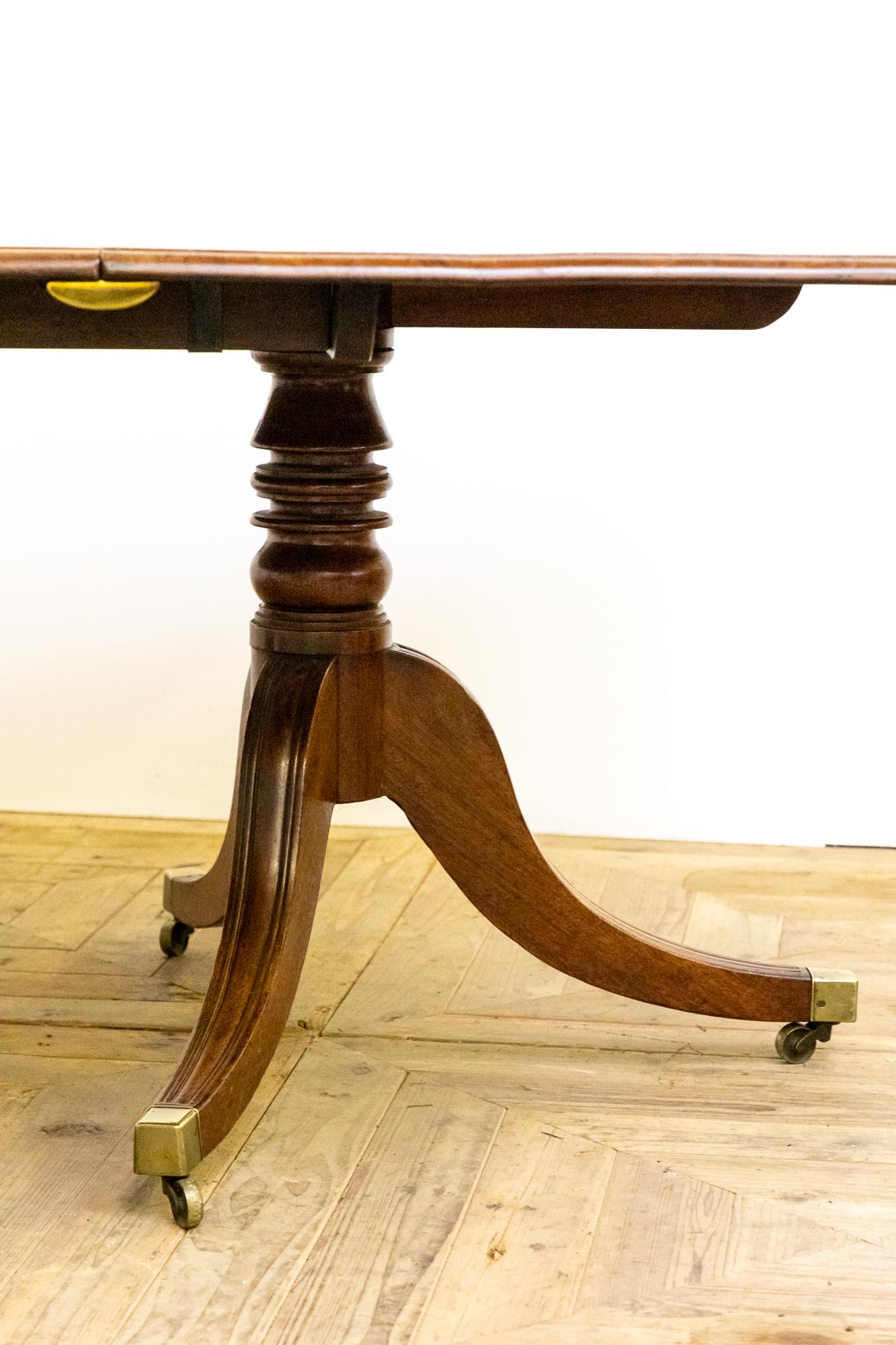 A stunning English country house dining table. Of traditional twin pedestal form and constructed entirely of mahogany with brass fittings. The pedestals have beautifully turned central columns above trio of sabre legs with reeded detail terminating