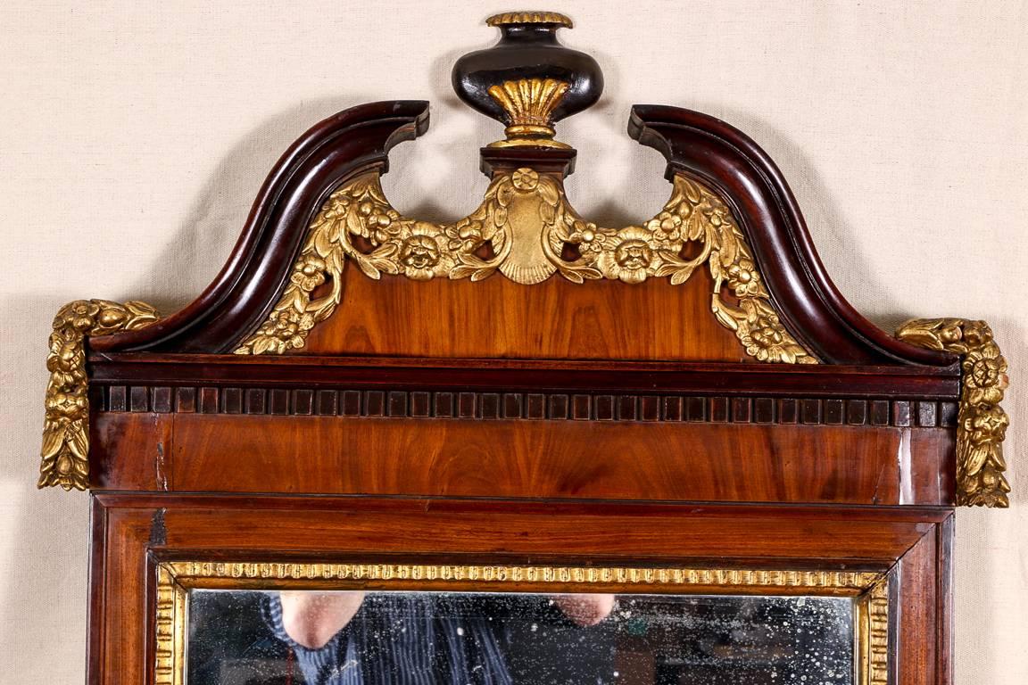 Antique 18th century George III pier mirror, carved mahogany with burled wood veneers, broken bonnet on top with urn finial, and decorated with a carved and gilt floral garland and a mahogany dentil frieze on the burled wood frame, mirror with a