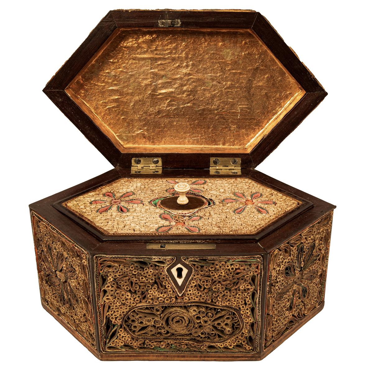 A good antique Georgian scrollwork tea caddy, circa 1780.
The caddy of hexagonal shape, the front, back & cover with overall decoration of paper scrolls in stylized floral & foliate motifs. The caddy having a hinged lid with a turned brass hinged