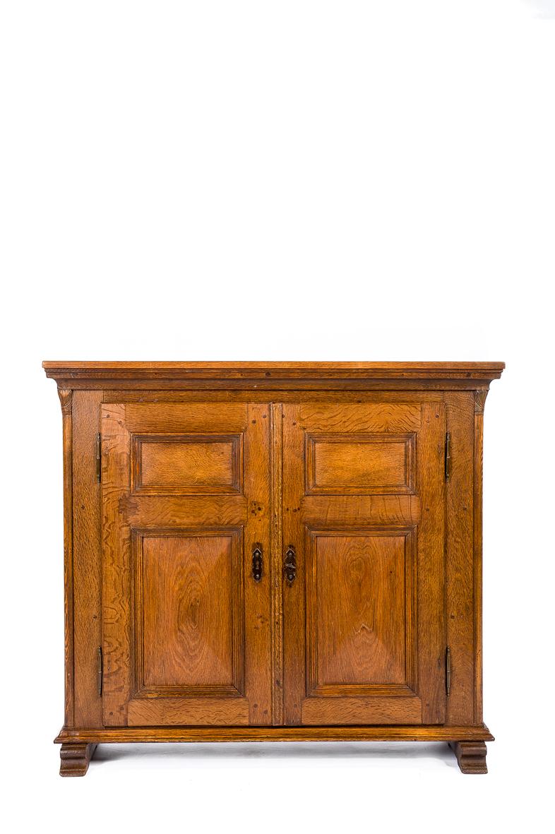 This elegant hall cabinet originates in Germany, in the region Nordrhein Westphalen. It was made in the finest quality European summer oak. The cabinet has two doors with every two recessed panels. The lowest panels are slightly diamond-shaped and