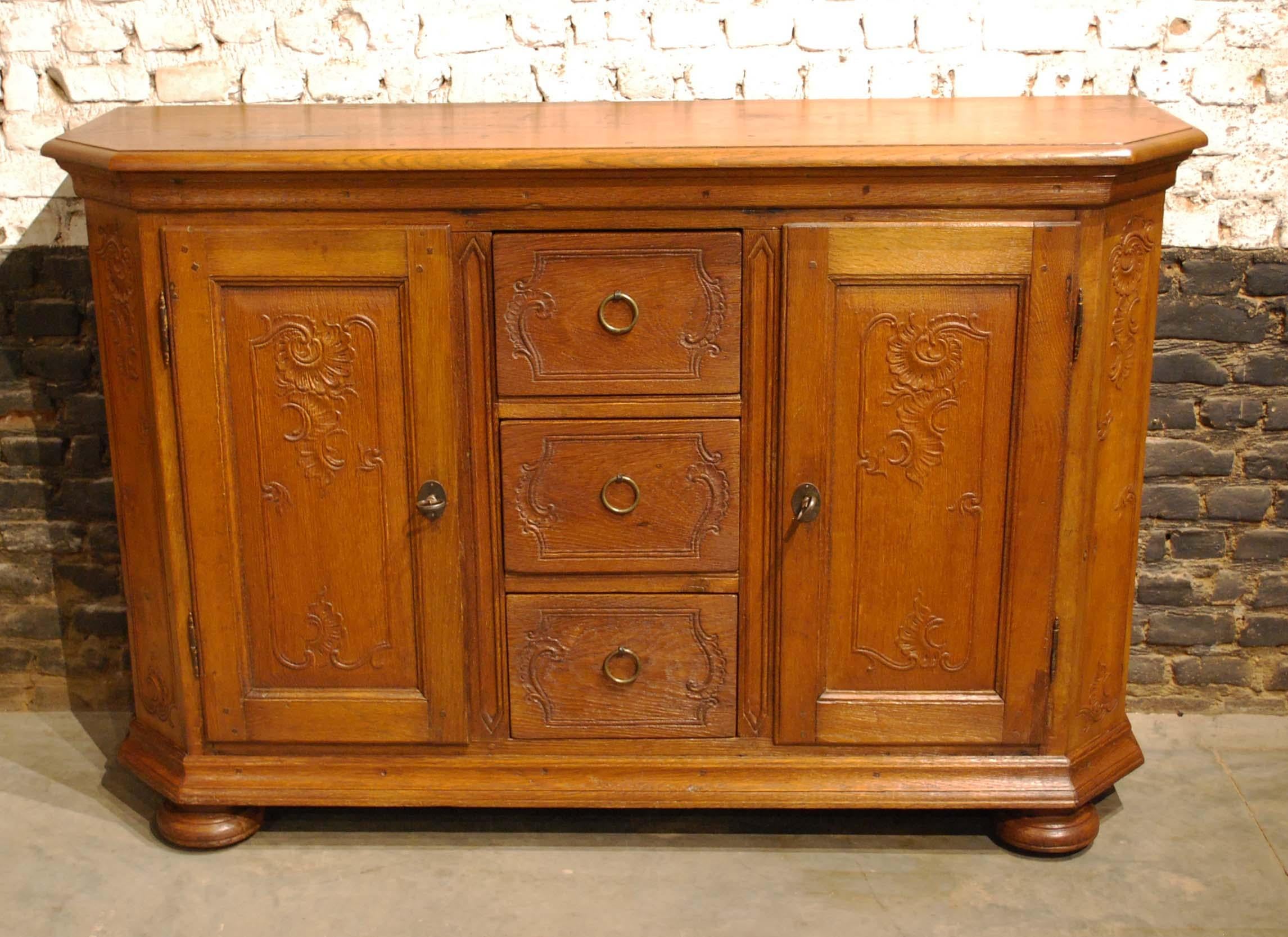 A beautiful honey color German oak dresser with two doors and three drawers. 
The cupboard was made in Germany in the Moselle region in circa 1780. The top has a bullnose profile and is joined to the base by the use of wooden pens. It has sweeping
