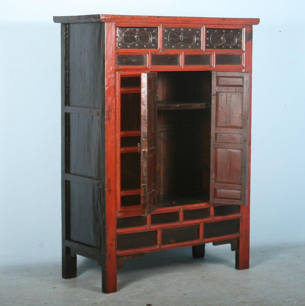 Visual intrigue abounds in this dramatic Chinese cabinet or armoire. It is the unique, heavily paneled bi-fold doors and upper drawers that one finds mezmerizing with the evocative red trim. A surprise awaits inside as well; note the interior bottom