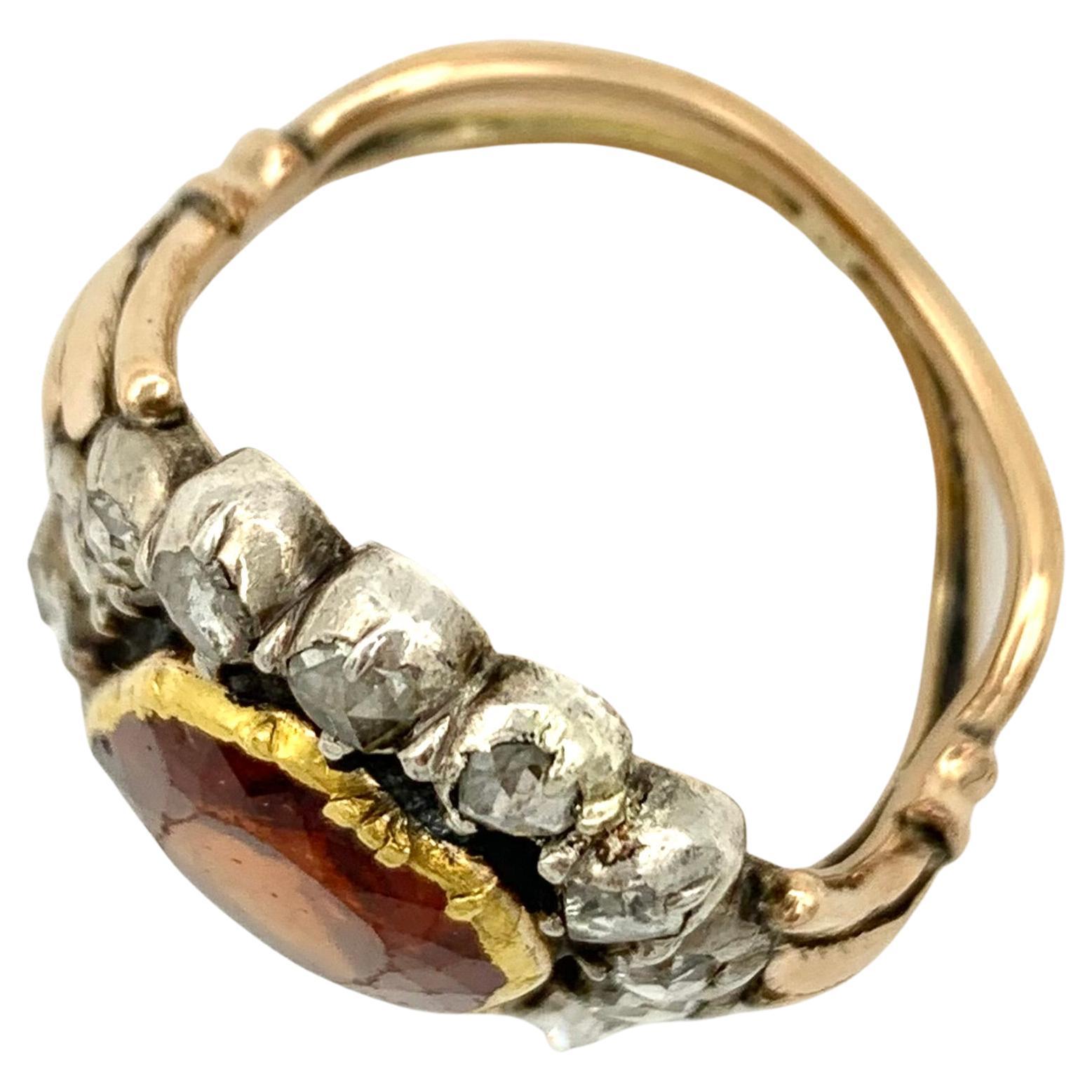 This large 18th century dress ring is set with a hessonite garnet mounted in gold and surrounded by fourteen rose diamonds set in silver. The back of the ring has been cut open in the course of history, most probably to remove dirt accumulated over