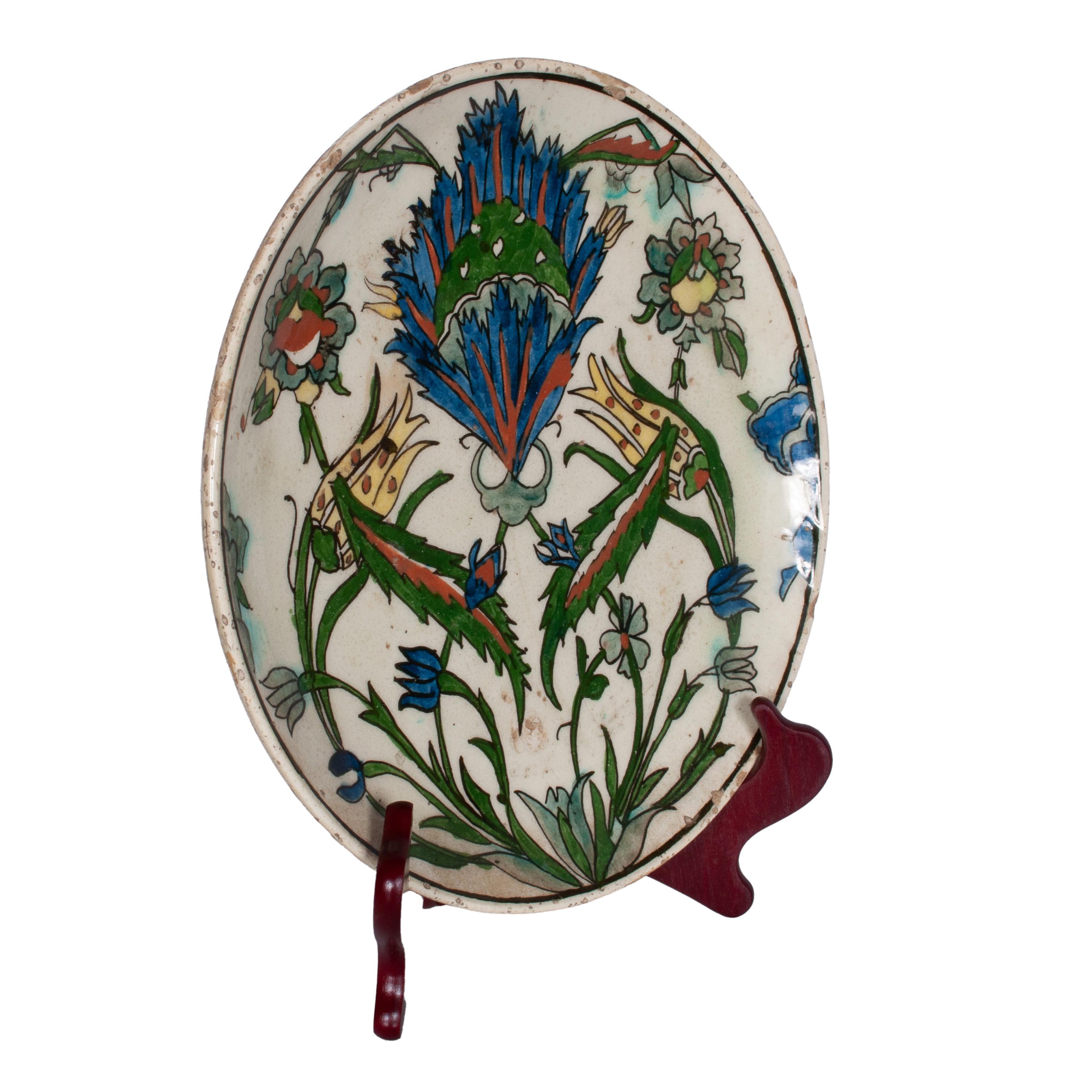 Une bonne assiette ancienne en poterie ottomane Iznik/Kutayha du XVIIIe siècle, vers 1750.
L'assiette a un fond en glaçure crème, peint à la main avec des motifs floraux multicolores en bleu sous glaçure, vert et rouge. L'assiette est décorée de