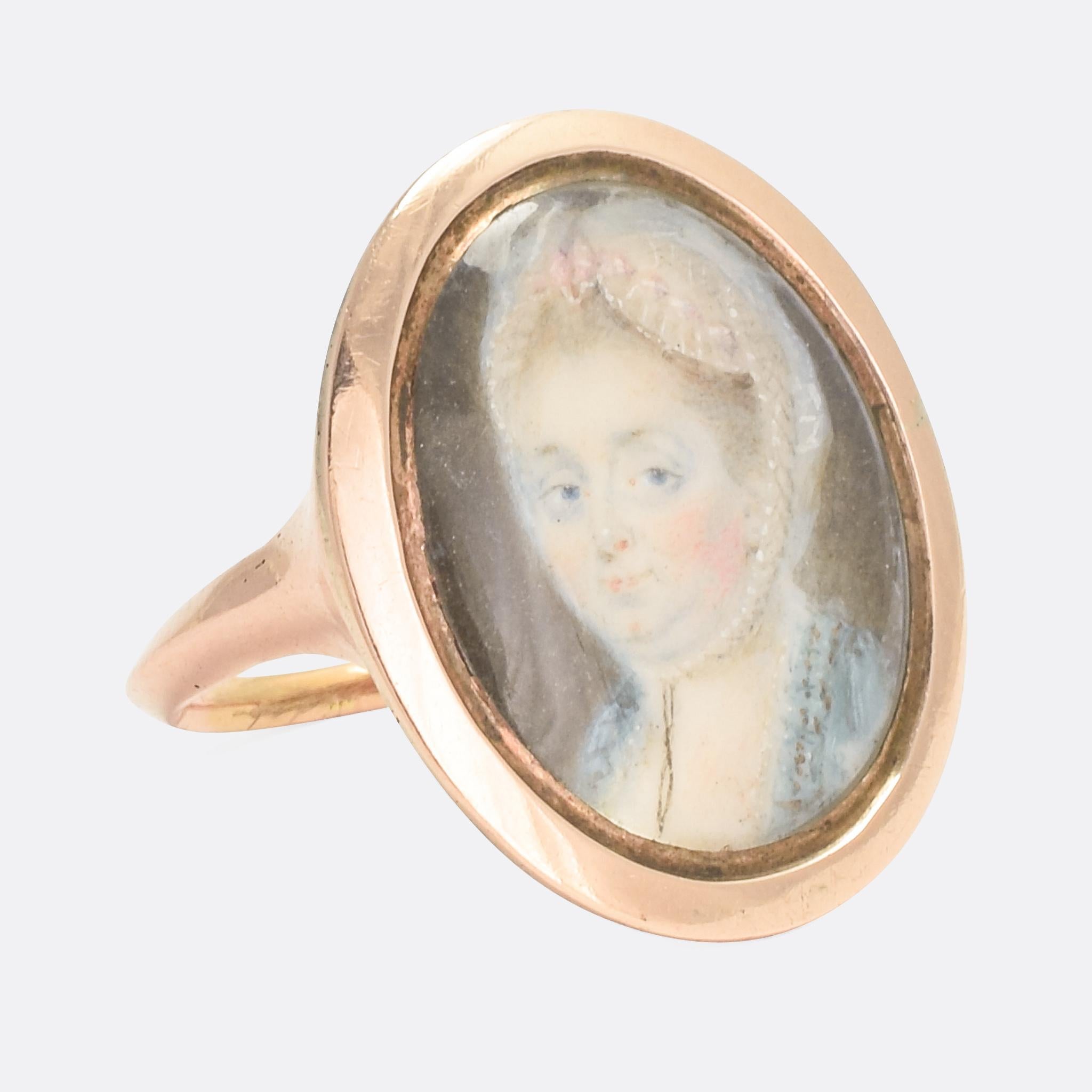 An 18th Century portrait ring depicting a lady wearing a turquoise coloured dress and lace bonnet. It dates from circa 1760; the detail to the miniature painting is wonderful, especially to her face and bonnet. Modelled in 15 karat rose gold, it