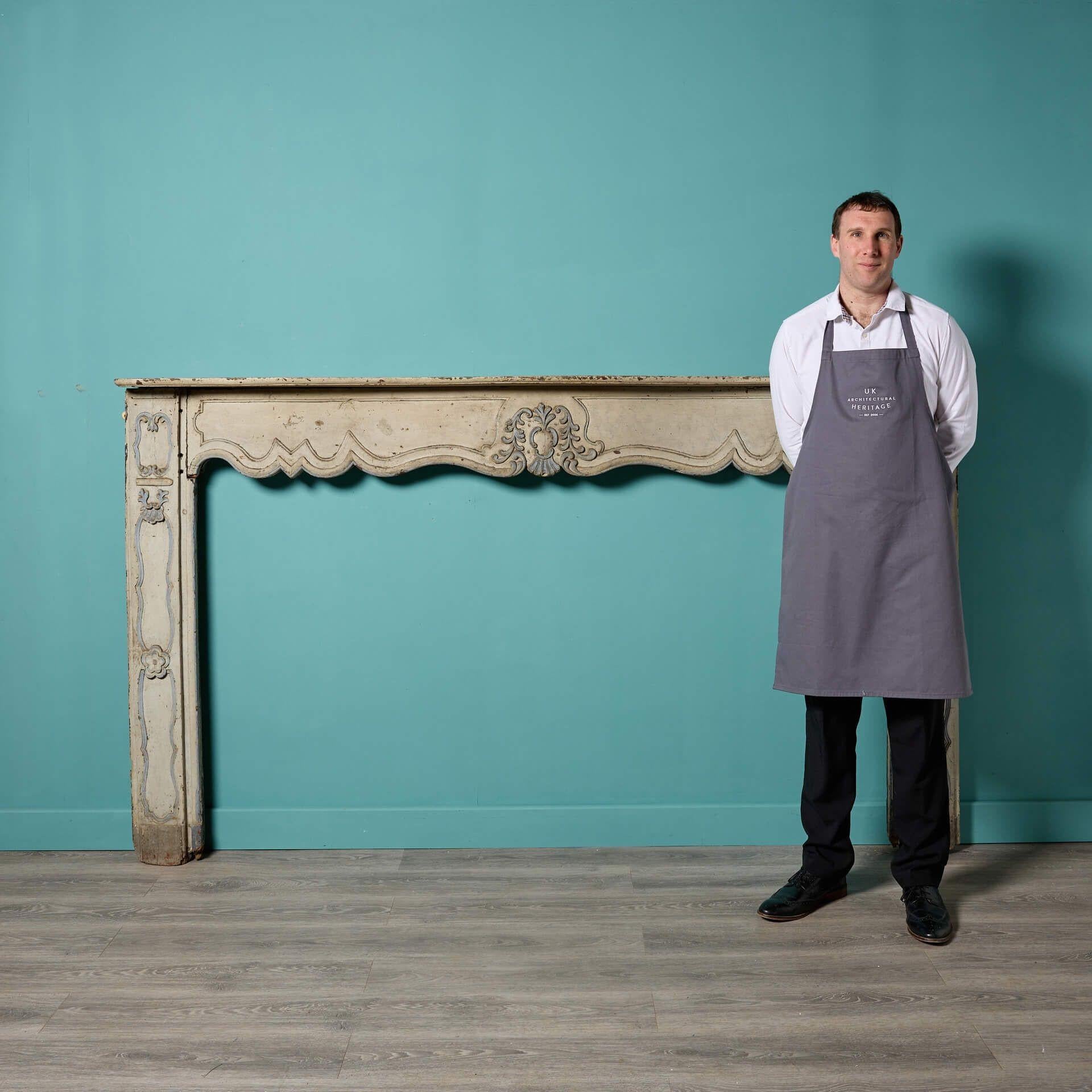 An antique early 18th century French painted oak fireplace in the manner of Louis XV. The shaped panelled frieze and jambs of this fireplace are surmounted by a serpentine shaped shelf, decorated with floral moulds.

This fire surround showcases the