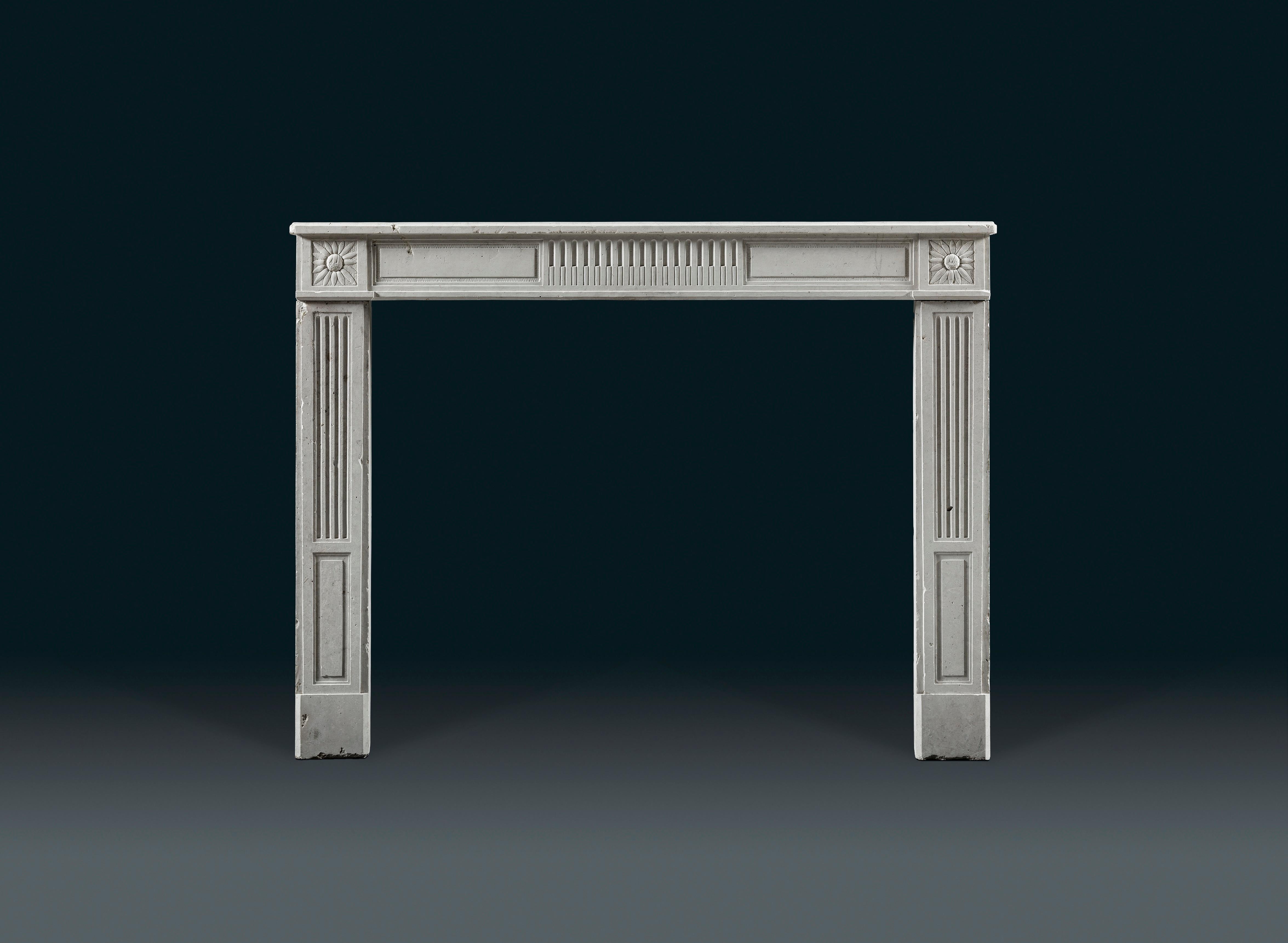 An antique 18th Century, French Louis XVI period, provincial stone fireplace. The simple rectangular moulded shelf above a frieze centred with a band of half filled finger flutes. This is flanked by inset fielded panels terminating in end blocks