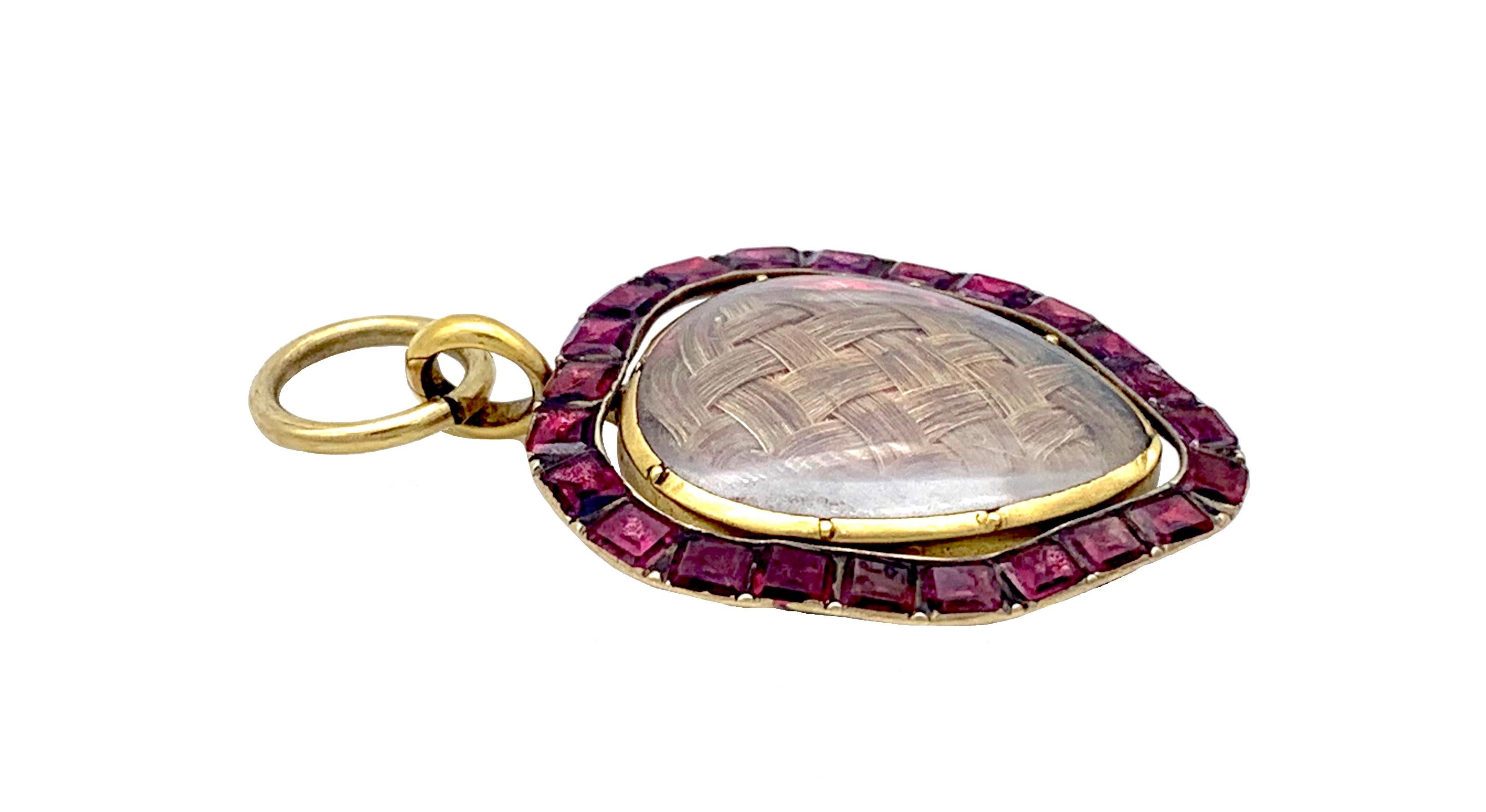 This beautiful heart pendant was hand crafted in the second half of the 18th Century. Within a heart shaped frame hand crafted out of gold and set with flat cut rectangular garnets we see an inner heart locket containing beautifully woven heart,