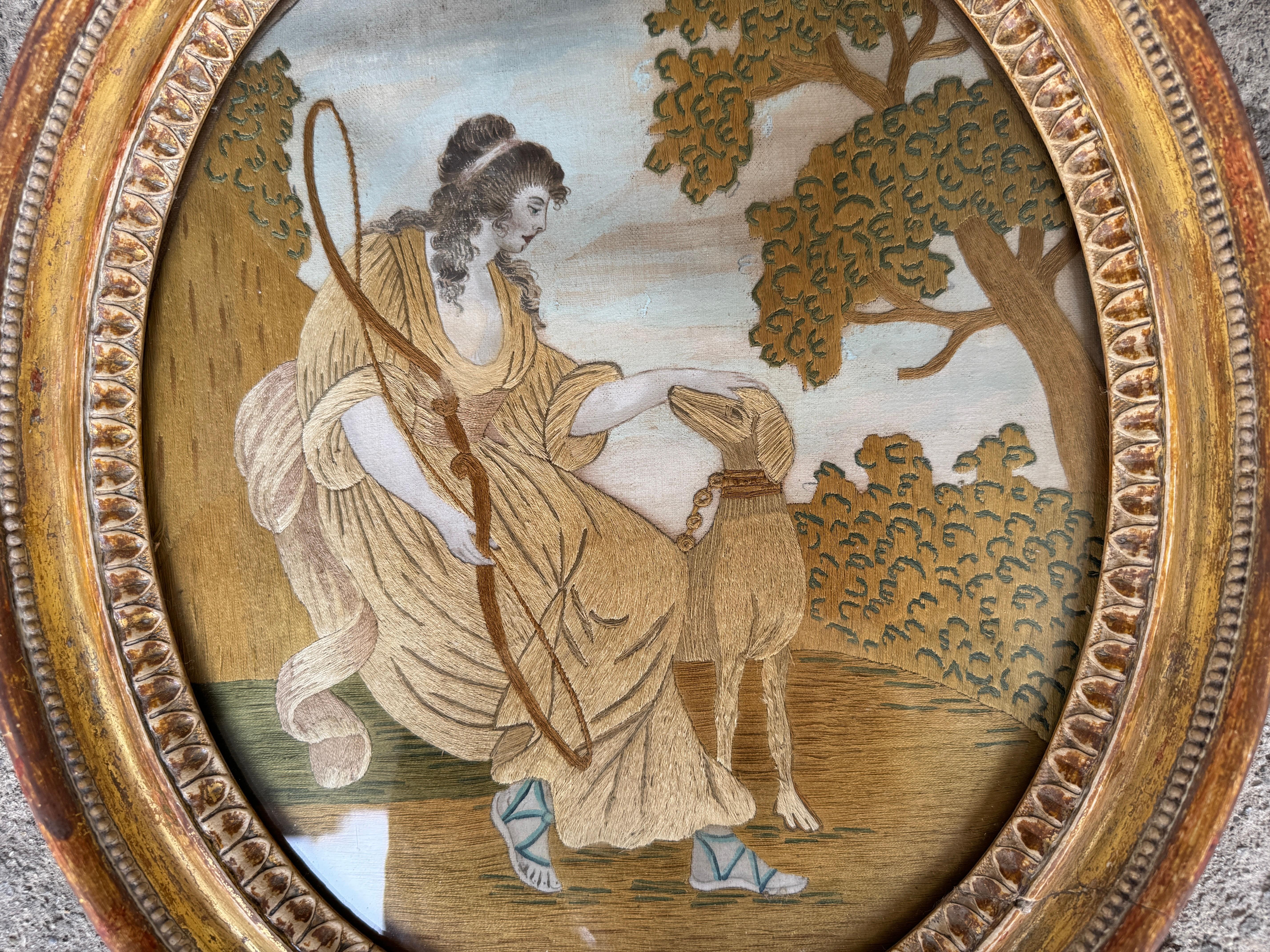 Dieses exquisite gestickte Gemälde wurde in den 1770er Jahren geschaffen.
Das Gemälde zeigt eine Jägerin und ihren Hund in einer ländlichen Gegend. Die Jägerin erkennen wir vielleicht als die Göttin Diana, die seit der Antike am häufigsten als