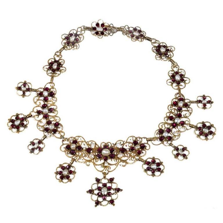 Openwork design to the baroque pearl and garnet surround.
39 cm lenght
Italian women have always loved lavish display. Even for the poorest, a rich show of jewellery was all important. Italian goldsmiths were expert at making a little material go a