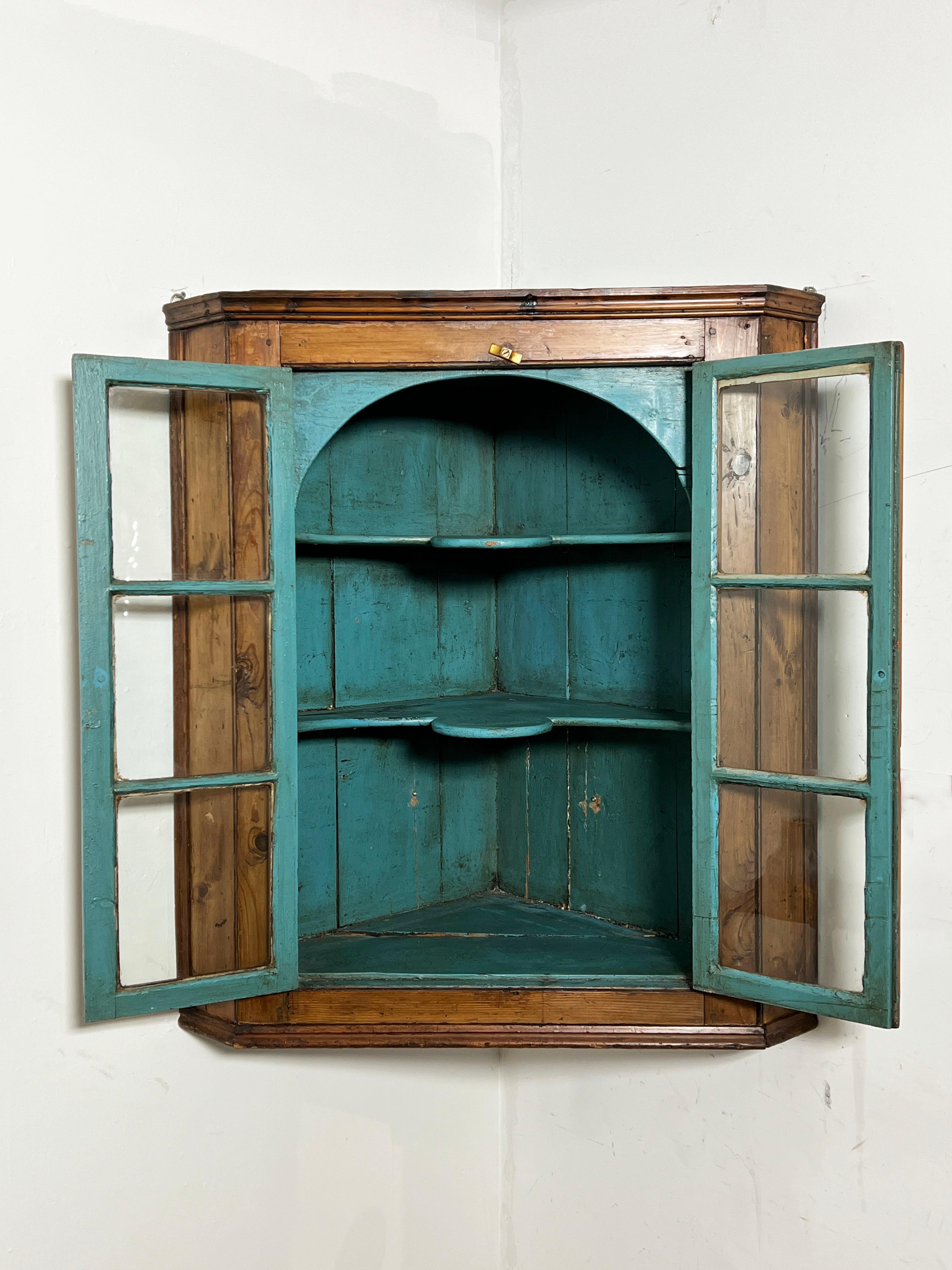 An 18th century New England hanging pine corner cupboard ca. 1760 with a Prussian-blue arched interior and paned glass doors.