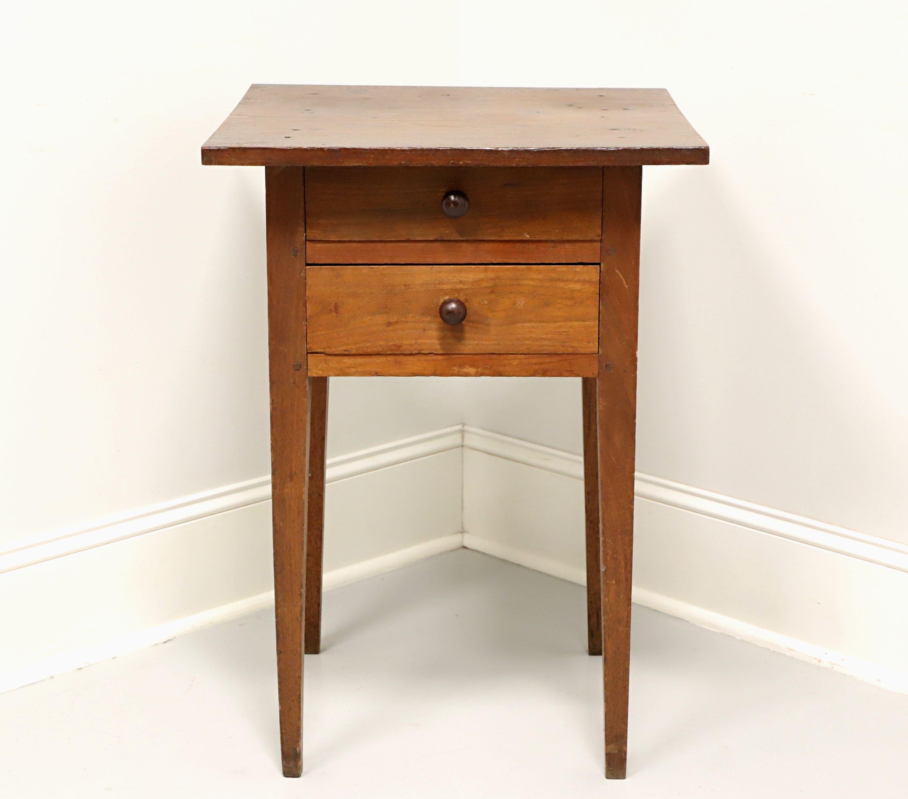 An antique 18th Century primitive side table, unbranded. Handcrafted of walnut, naturally distressed from age, polished wood knobs and tapered straight legs. Features two drawers of clout nail construction, top drawer having a fixed divider. Likely