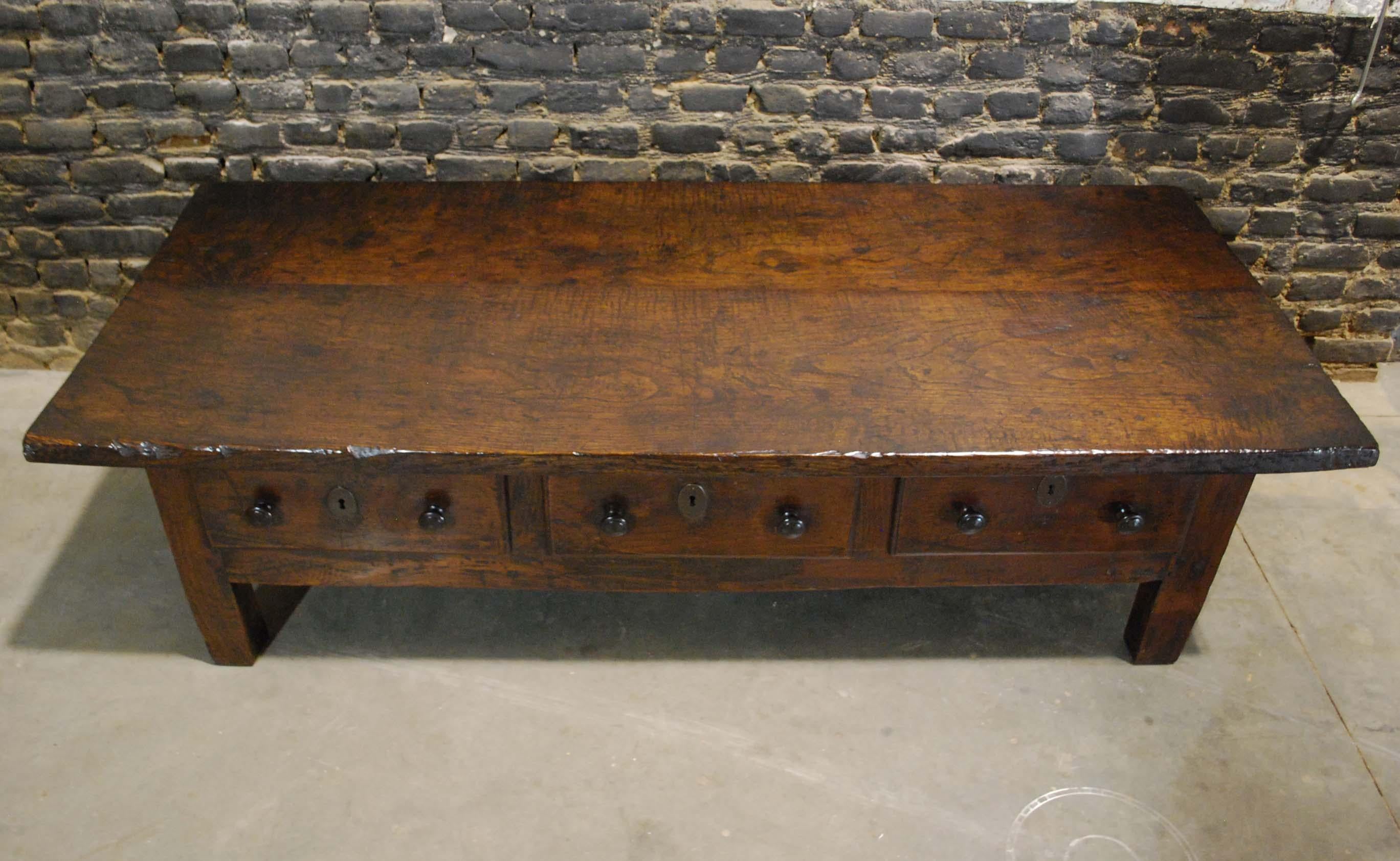 An early and rustic Spanish low table or coffee table that originates in Spain. The tabletop is 1.5 inches thick and made of two wide pieces of solid chestnut timber with a beautiful wood grain pattern. The table has three drawers with oval forged