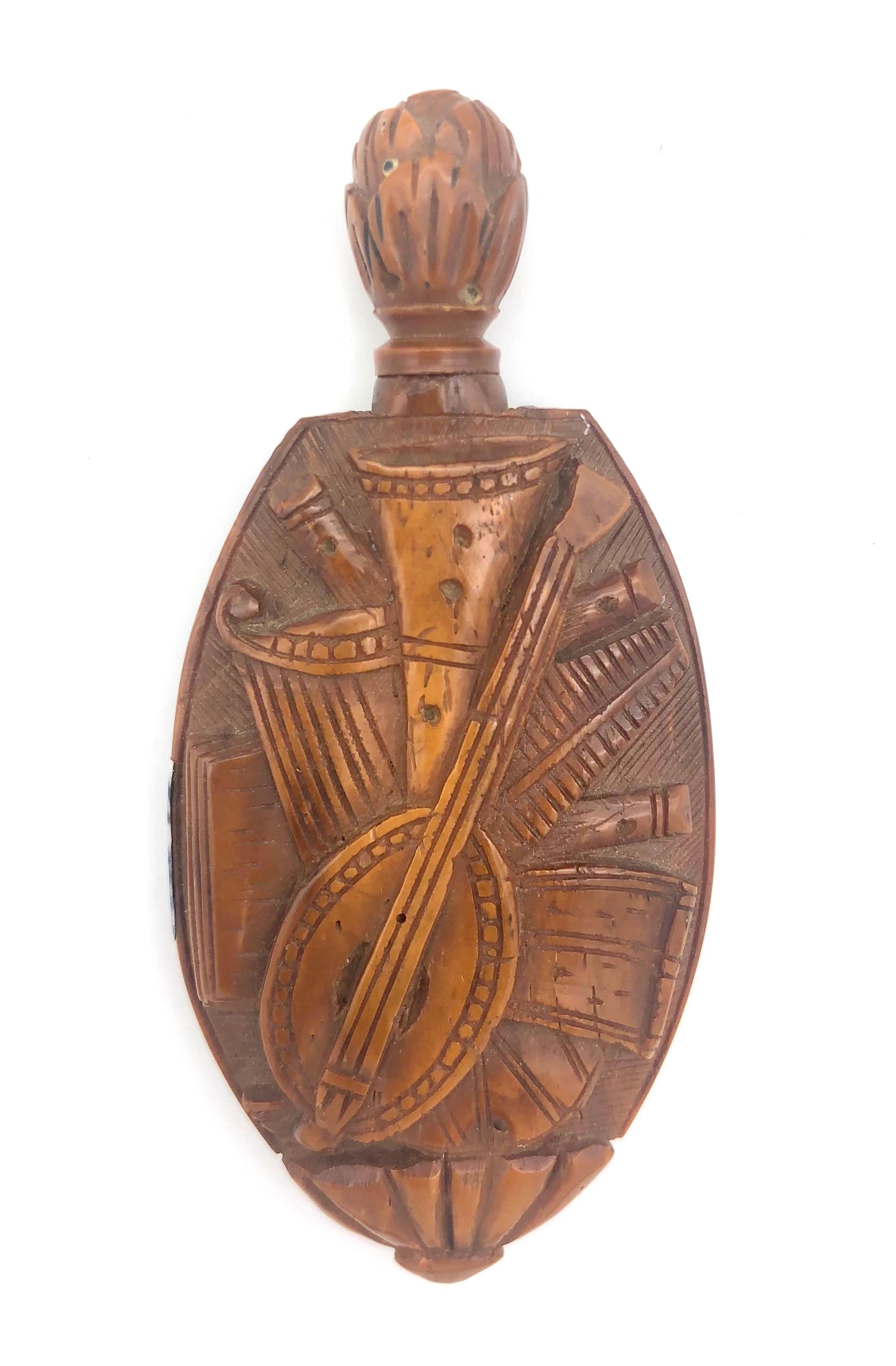 This snuff bottle was carved out of  walnut in the last quarter of the 18th century. One side of the object is decorated with two dogs and hunting regalia, the other with musical instruments. We can make out a flute, a gitar, a lyreand a horn. 
