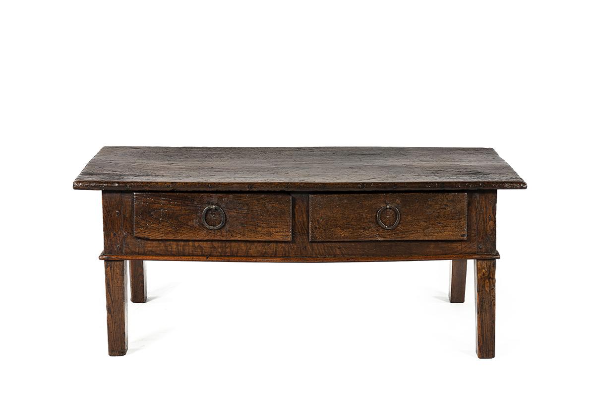 Esta mesa de centro con carácter se fabric�ó en España durante el siglo XVIII y está hecha totalmente de madera maciza de castaño. Refleja la artesanía rústica y honesta típica del mobiliario rural español de la época.
El amplio tablero de la mesa