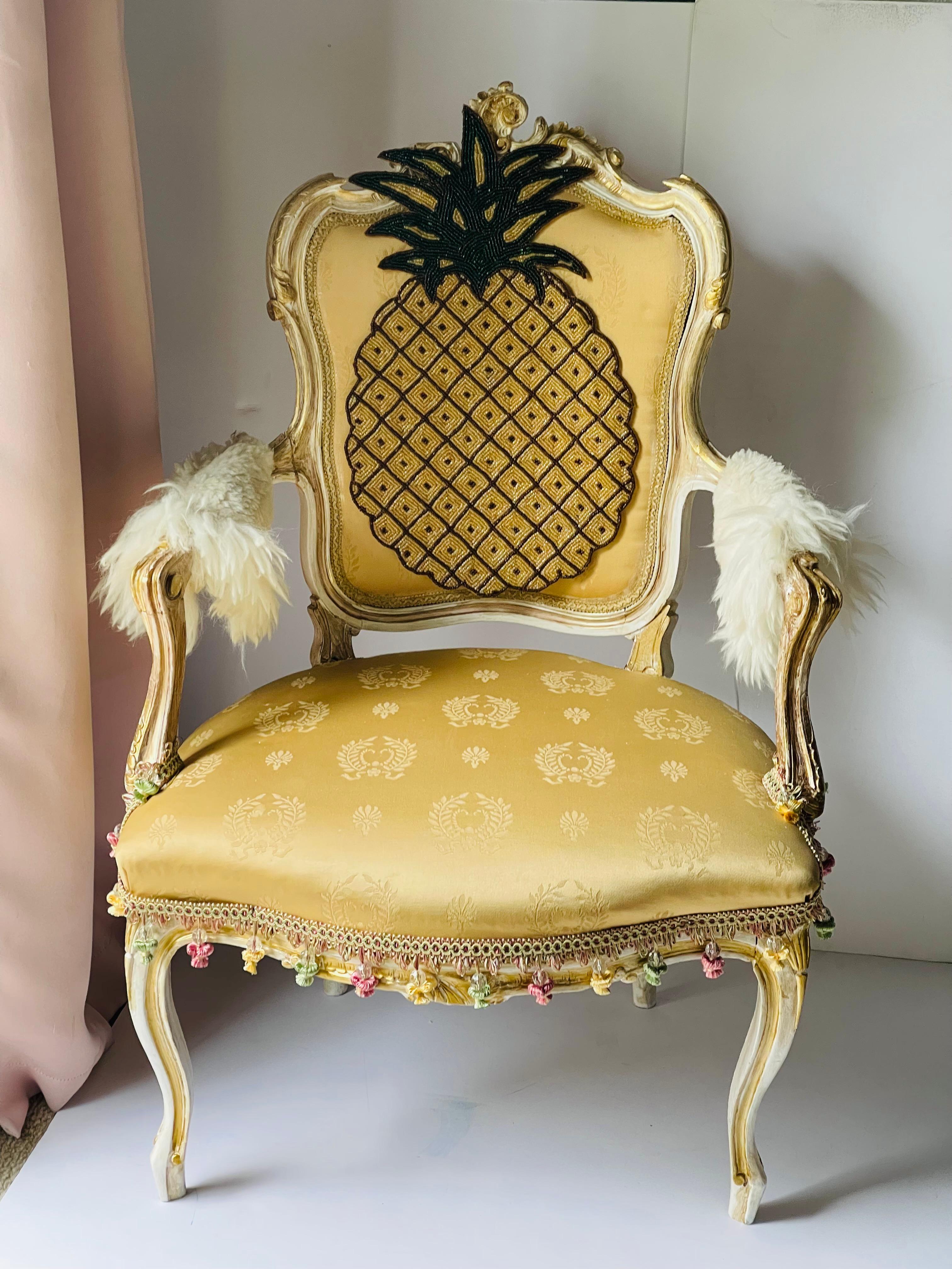 Ancien fauteuil du C.I.C. en noyer sculpté à la main, peint en blanc antique et or, finition vieillie. Redessiné avec un ananas perlé, des franges perlées et des manches en peau de mouton.