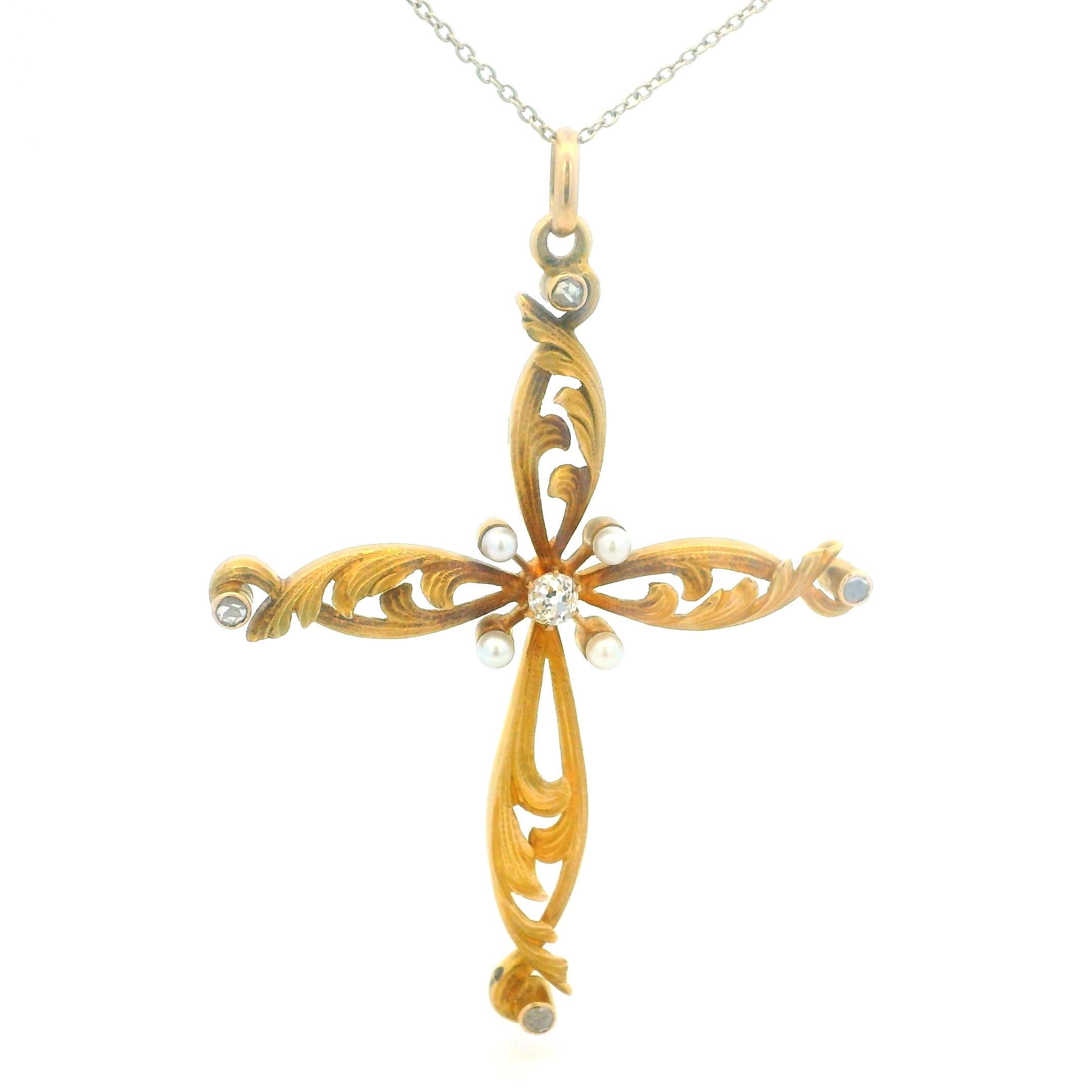 Un elegante ciondolo a croce antico, risalente ai primi anni del 1900, finemente realizzato in oro giallo 18 carati con delicati dettagli a foglia traforata. Al centro si trova uno scintillante diamante vecchio taglio europeo, con altri quattro