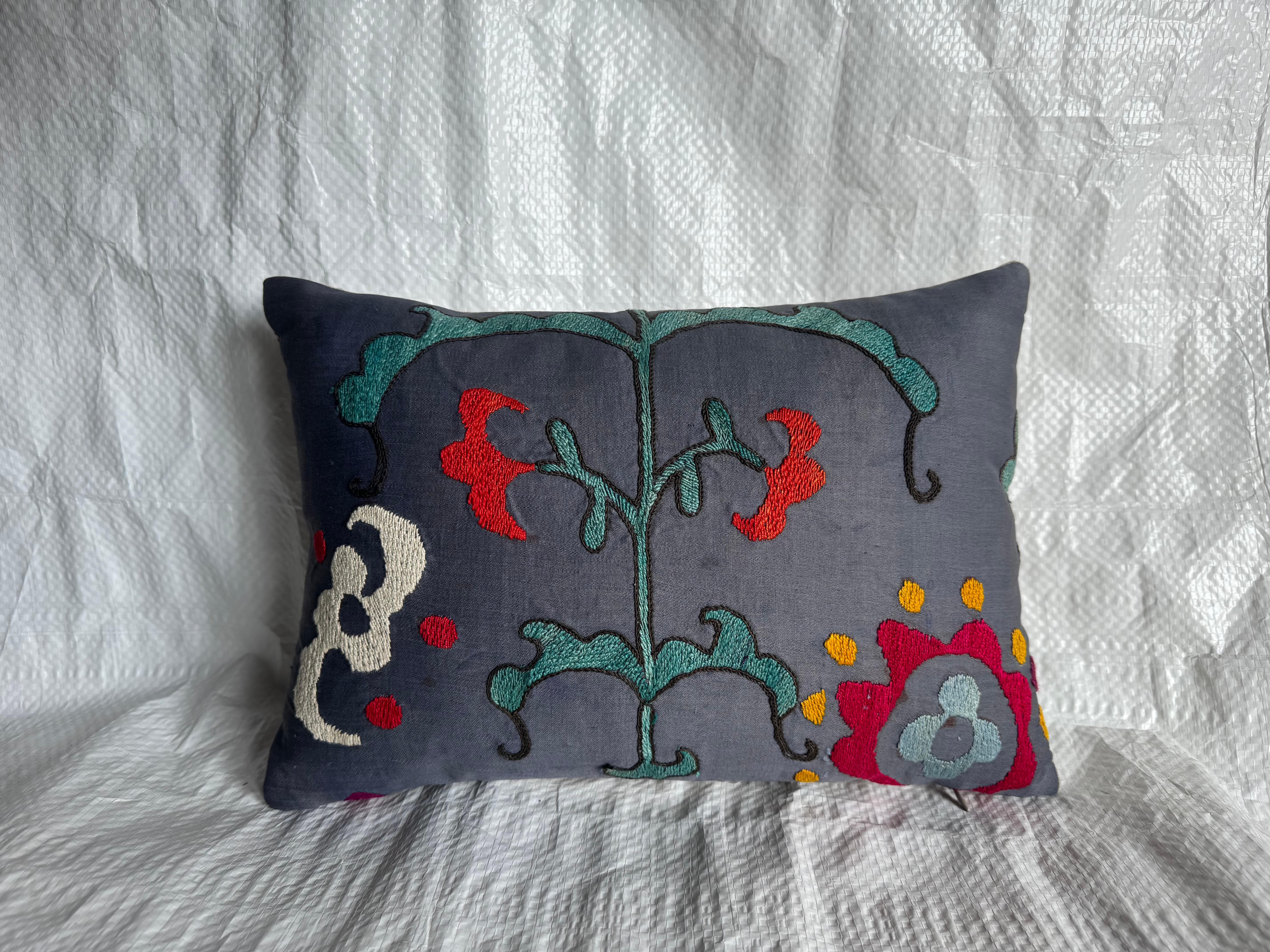 A beautiful 1900s antique Suzani pillow showcasing vivid floral embroidery on a deep charcoal-gray ground. This hand-embroidered piece features bold motifs in red, teal, ivory, and mustard yellow — characteristic of traditional Central Asian Suzani