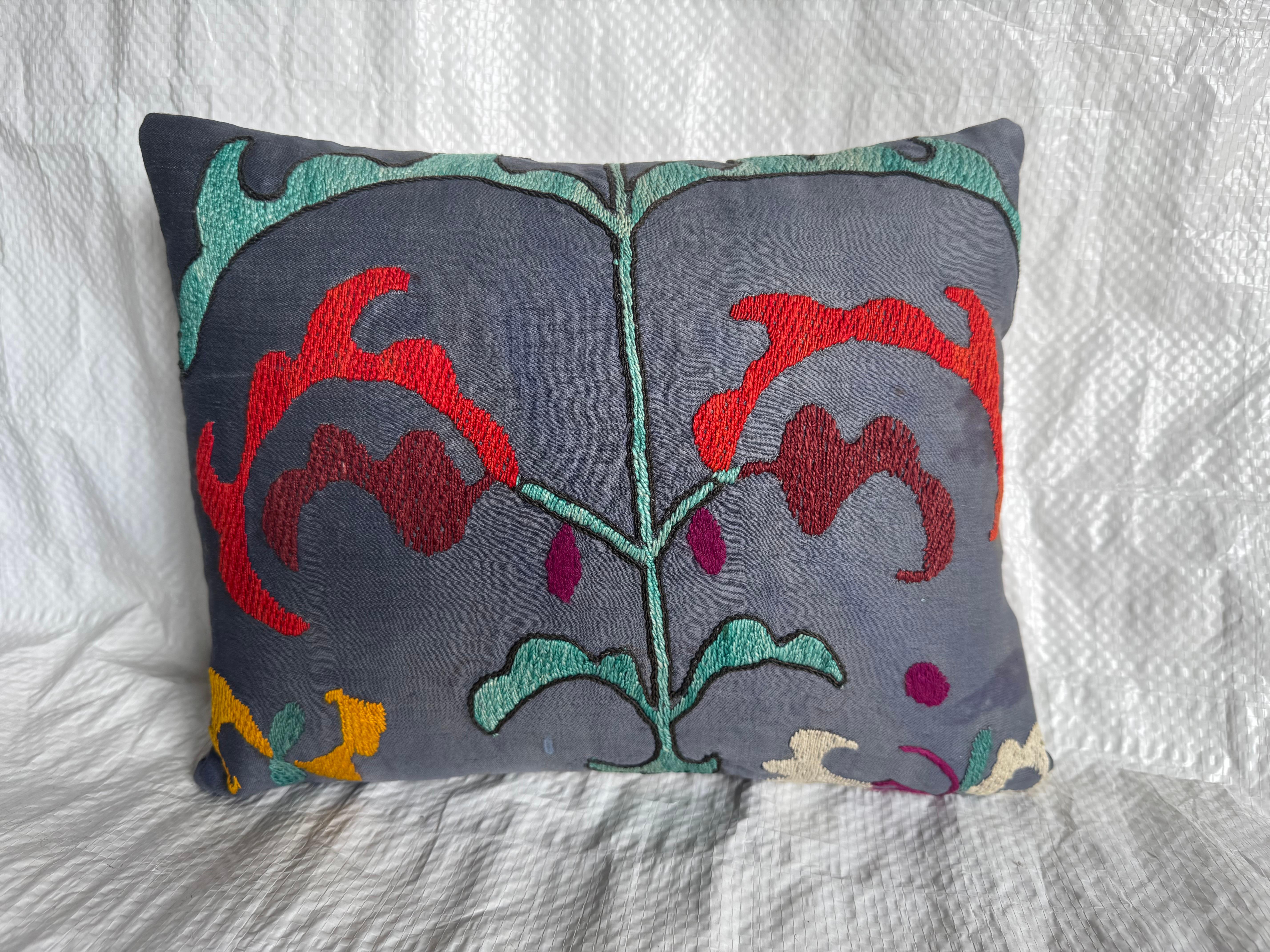 A striking antique 1900s Suzani pillow showcasing vivid hand-embroidered floral motifs in deep red, teal, mustard, and ivory threads on a rich charcoal-gray ground. This pillow was crafted from an authentic early 20th-century Suzani textile,