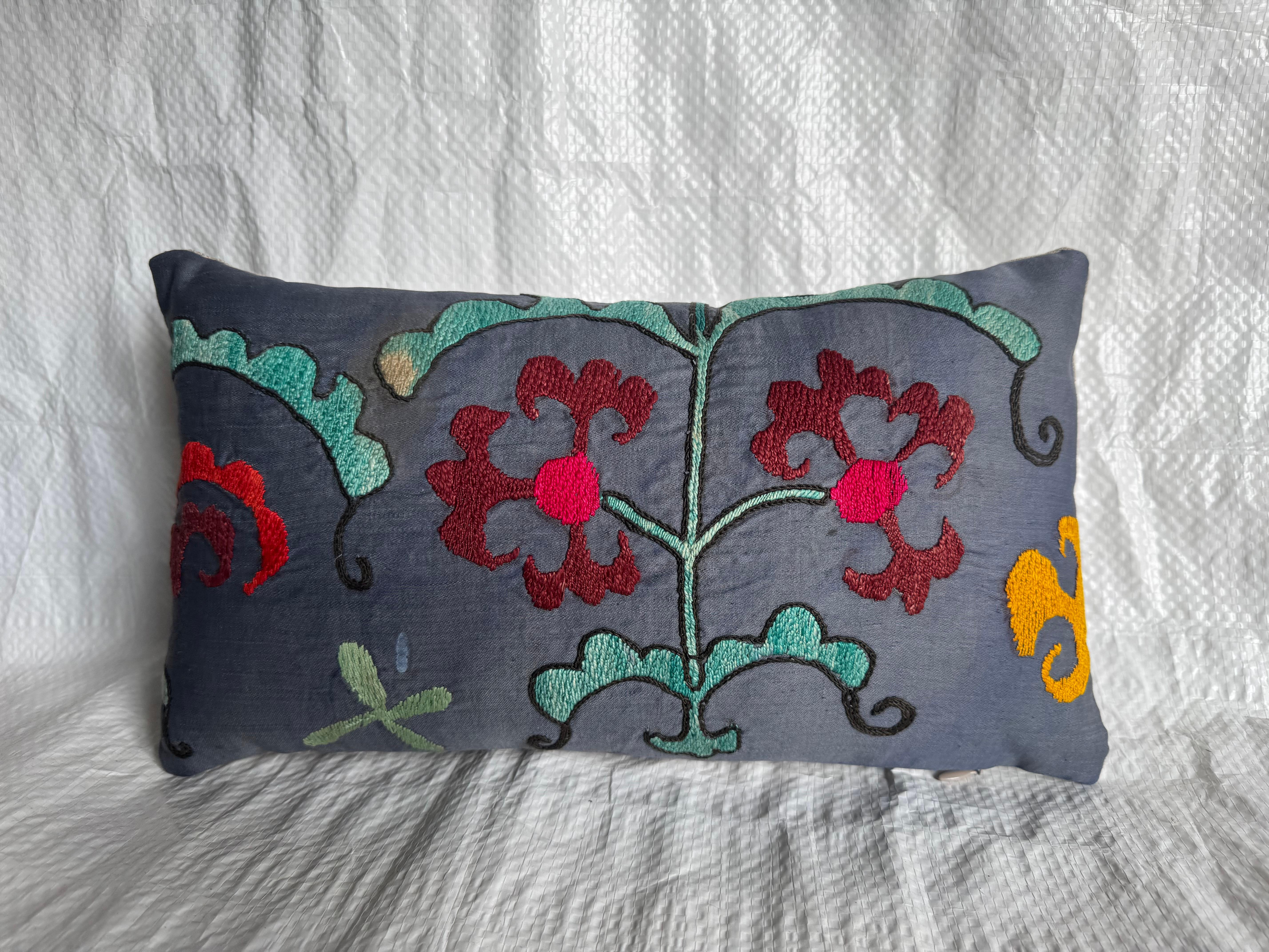 A beautiful antique 1900s Suzani pillow hand-embroidered with vivid floral and vine motifs in crimson, teal, mustard, and soft ivory on a charcoal-gray base. This early 20th-century textile was originally part of a larger Central Asian Suzani — an