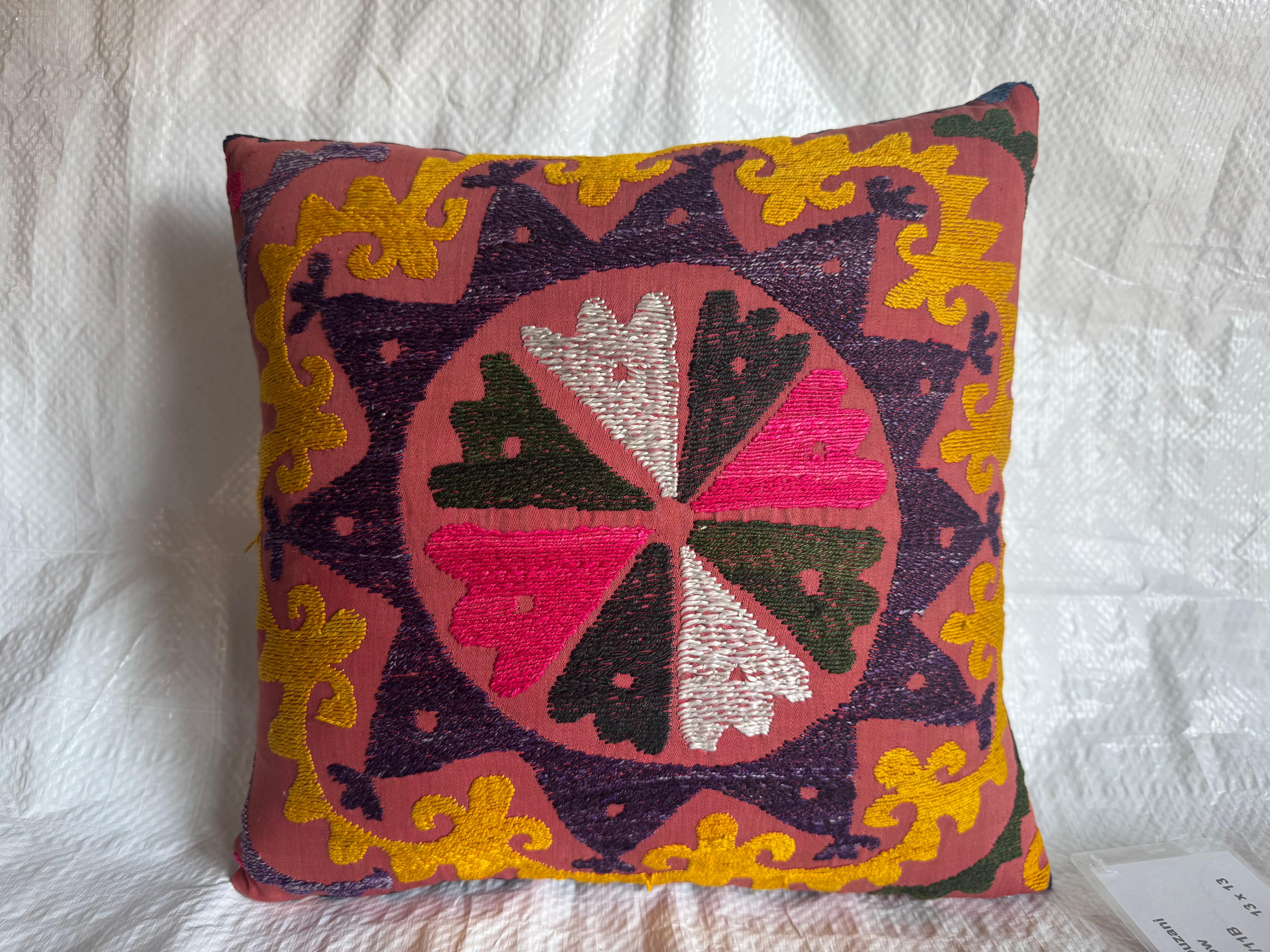 Ce coussin Suzani des années 1900 présente un médaillon en forme d'étoile entouré de motifs tourbillonnants brodés de jaune d'or, de prune, d'émeraude et de fuchsia. Chaque segment de pétale est méticuleusement brodé à la main avec des techniques