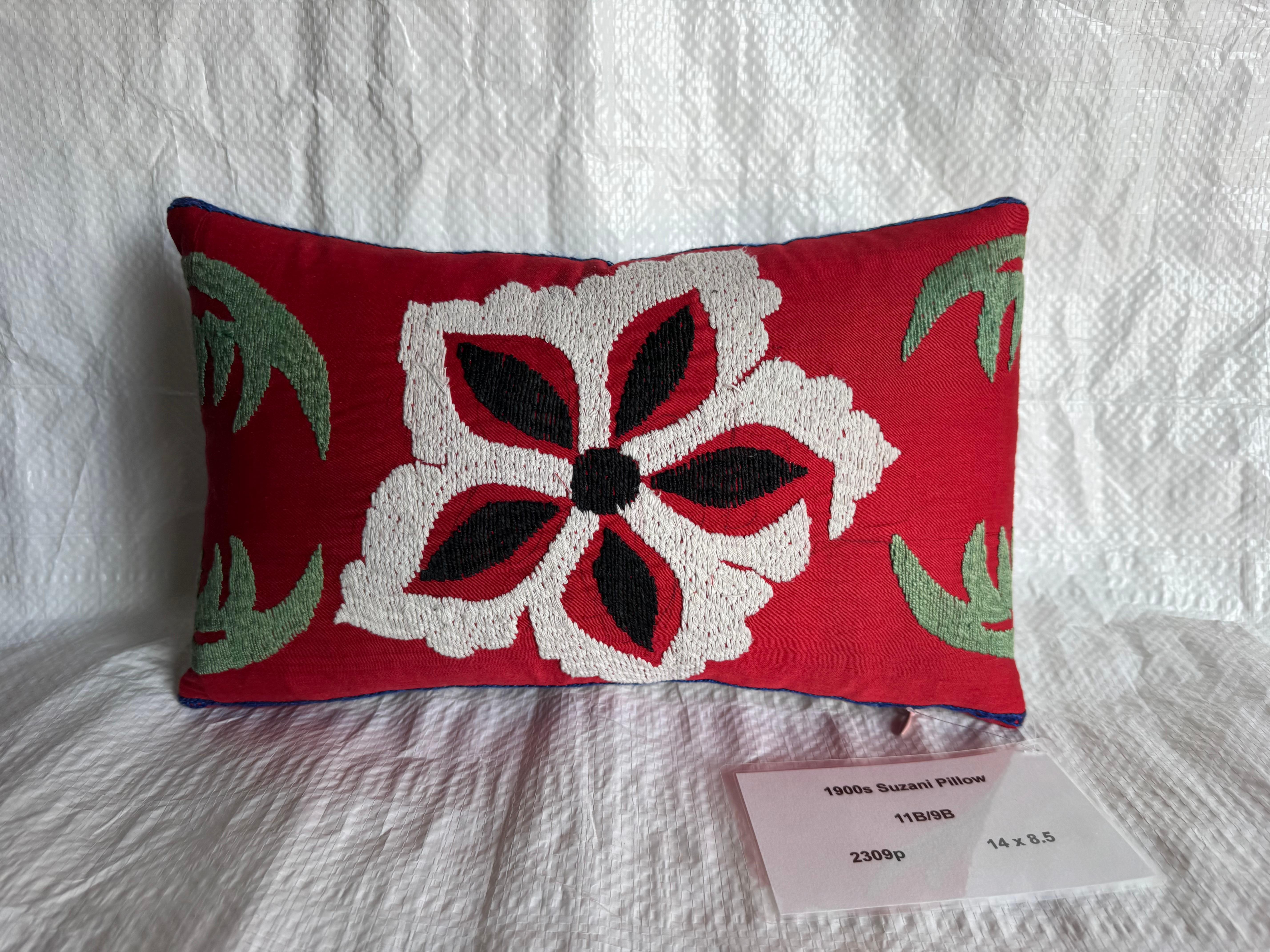 Un exquis coussin Suzani du début des années 1900 présentant un champ rouge frappant avec une broderie florale ivoire et noire audacieuse, accentuée par des détails verts doux. Brodé à la main sur du coton à l'aide de techniques d'aiguille