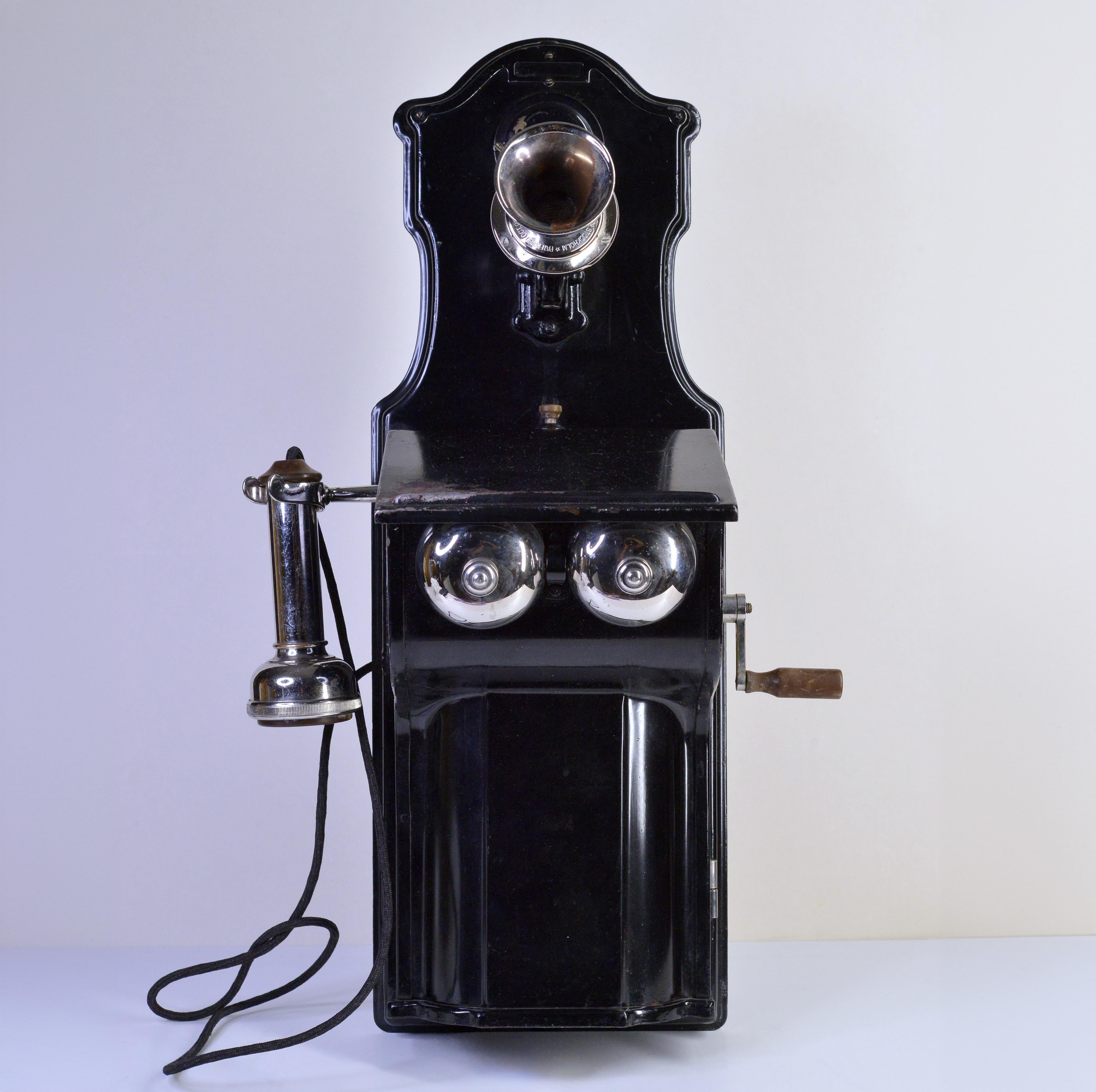Telefono della stazione ferroviaria svedese, AB L.A. Ericsson & Co. Stockholm, tipo AB 2100-2120, visto nel catalogo prodotti del 1911, in lamiera d'acciaio laccata nera, con bocchino fisso e auricolare RD 600 a polo lungo. Realizzato nel 1912 da M.