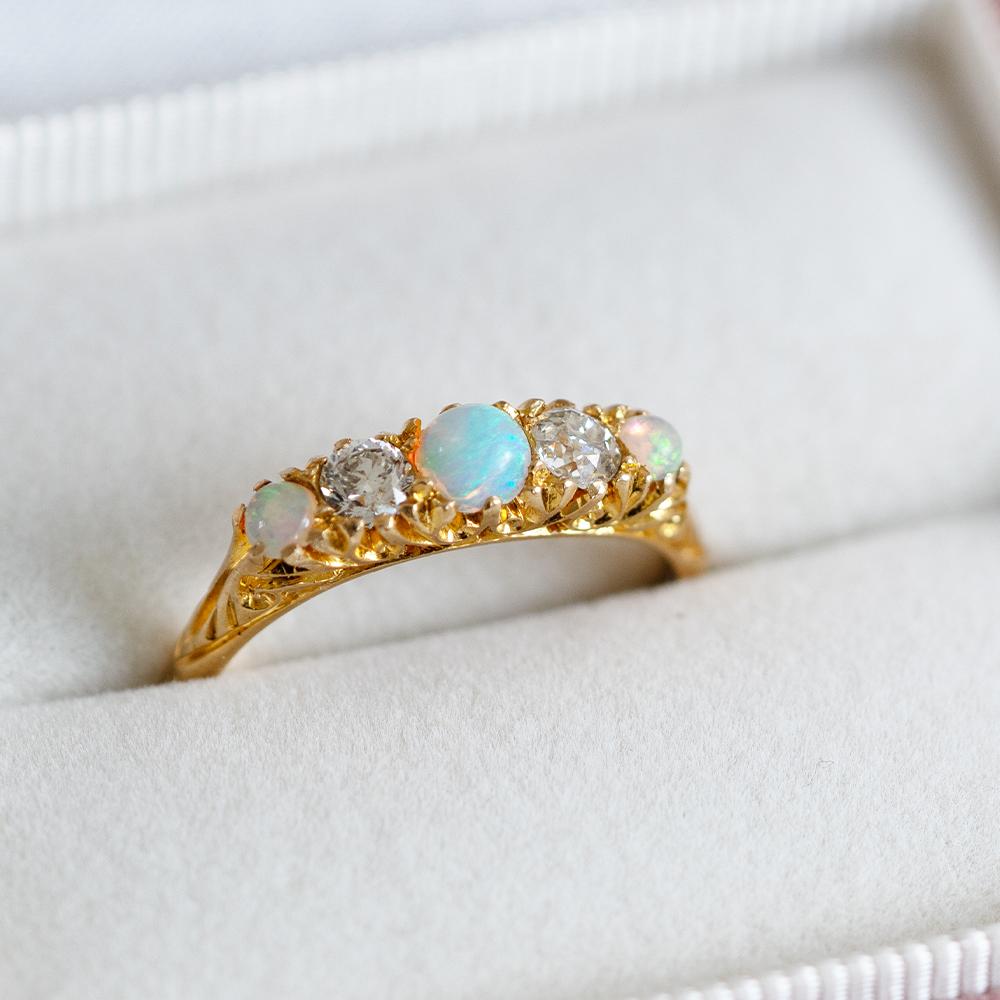 Questo squisito anello dell'epoca edoardiana, con marchio del 1915, presenta un'incandescente composizione di opali e diamanti antichi in una montatura d'oro finemente dettagliata. Al centro, un opale luminoso mostra lampi di blu, verde e rosa,