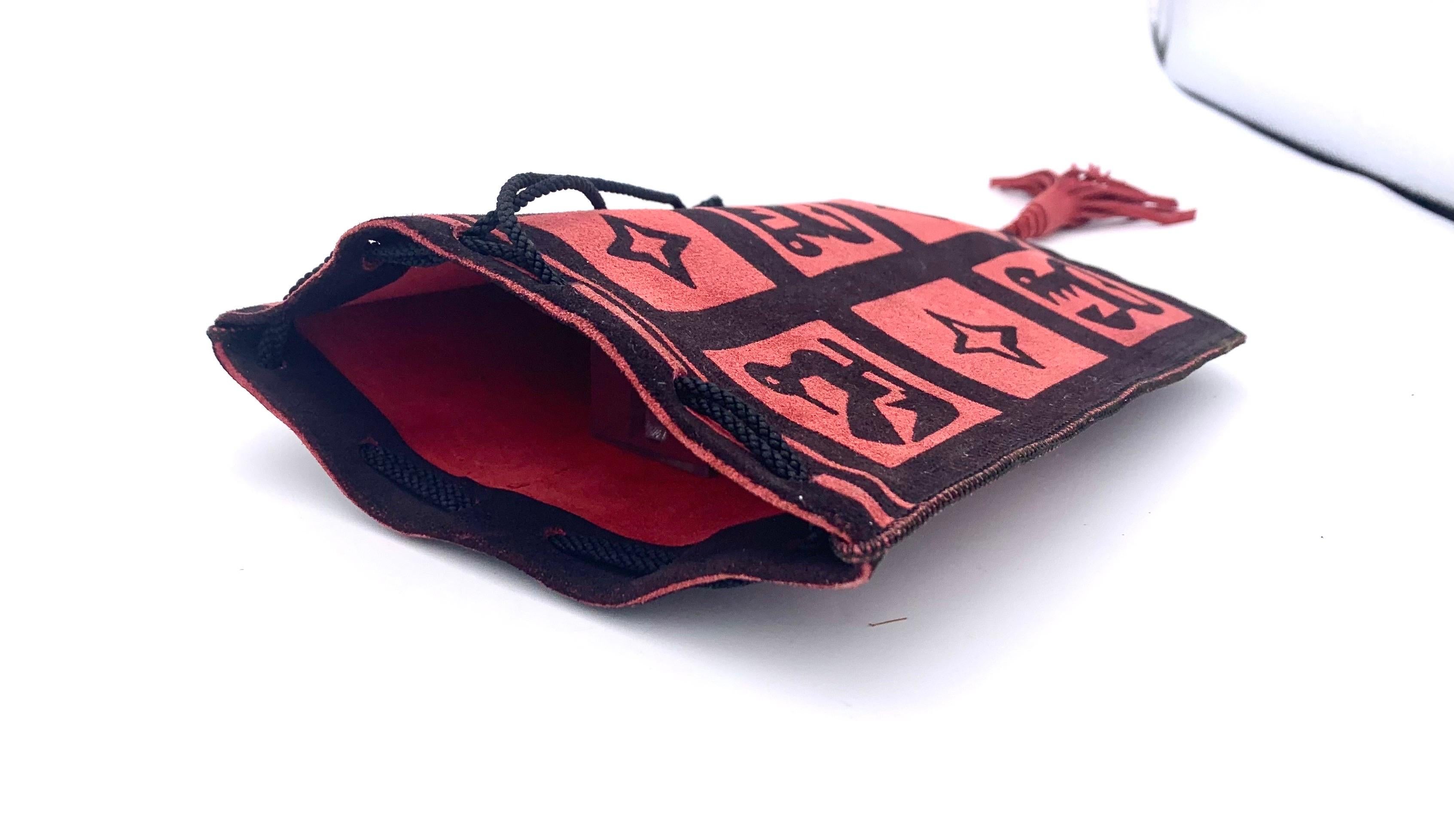 Este bolso Art Déco está hecho de ante rojo y estampado con adornos futuristas negros, algunos de los cuales parecen pájaros. Cada lado de la bolsa presenta nueve cuadrados, cuatro de los cuales están decorados con 4 estrellas dentadas. El bolso