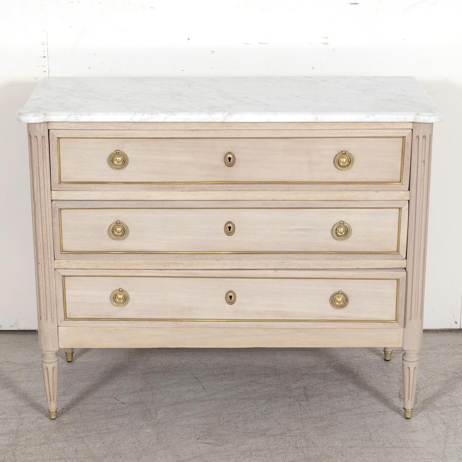 An early 20th century French Louis XVI style three-drawer mahogany commode handcrafted in Paris, circa 1920s, having a bleached or washed finish featuring the original Carrara marble top with cookie cutter corners over three full size drawers