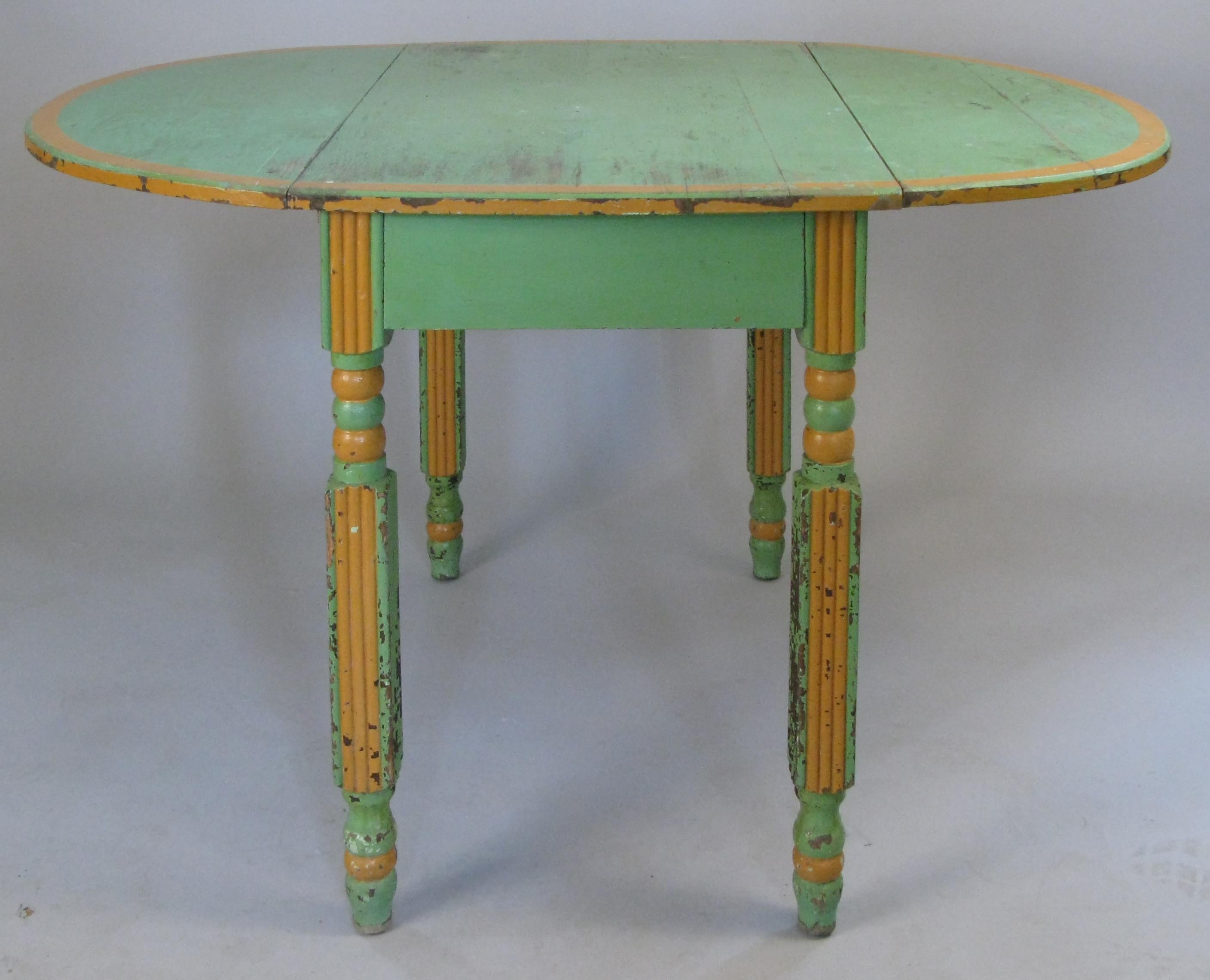 A very charming antique 1920s drop leaf dining table, in its original hand painted finish in light fern green with orange details. Turned legs and folding metal brackets to support the leafs when extended.