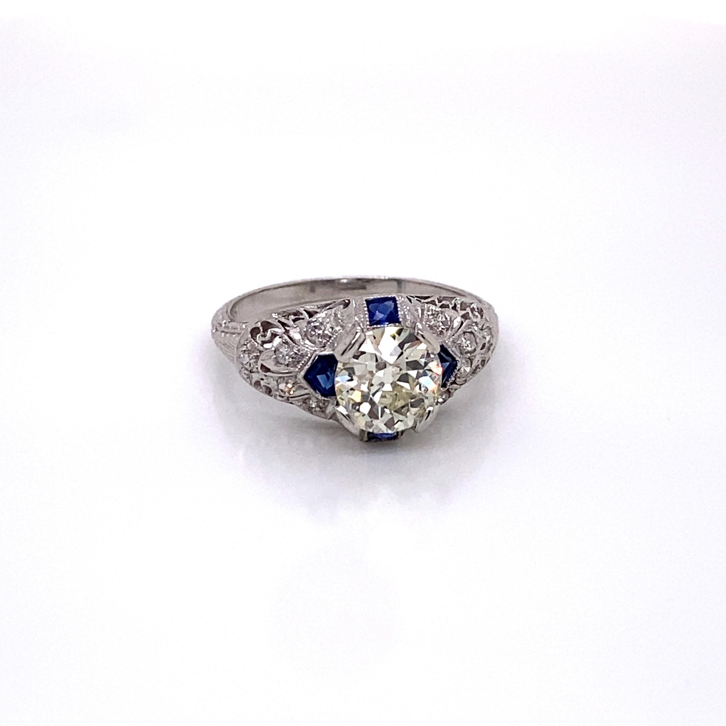 Antique 1920s Old European Cut Diamond Platinum Ring - then center diamond weighs 1.45 and is M color and VS1 clarity. Two French cut square sapphires and two French cut shield sapphires are bezel set on the North-South-East-West. Ten single cut