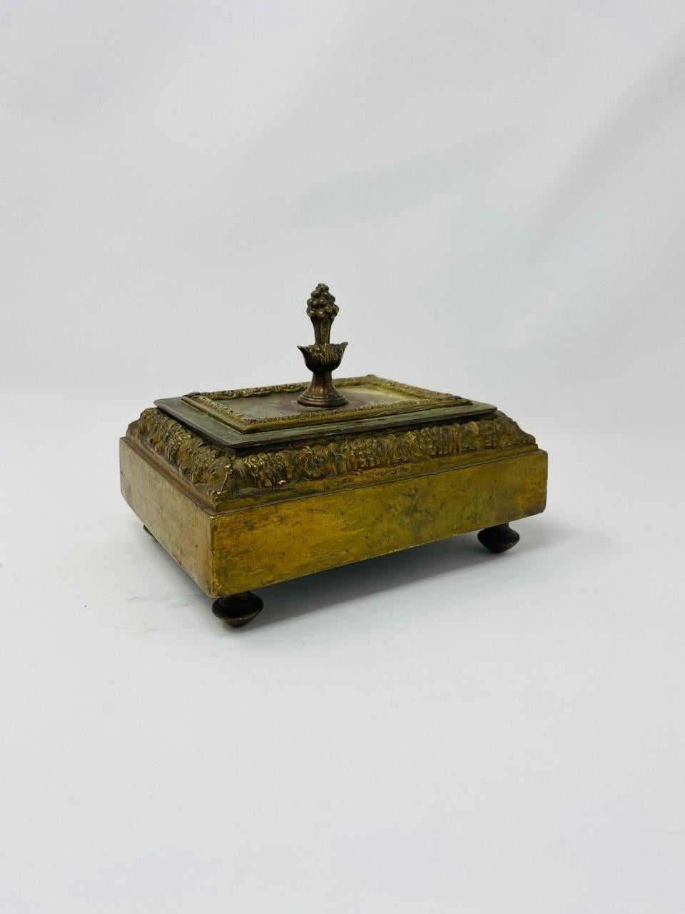 This fine antique of Austrian or possibly German bronze, stands raised on four feet with a finial cover that opens to a generous storage space. This box brings elements of the changing style of the 1920s with symmetry and severe lines in the body of