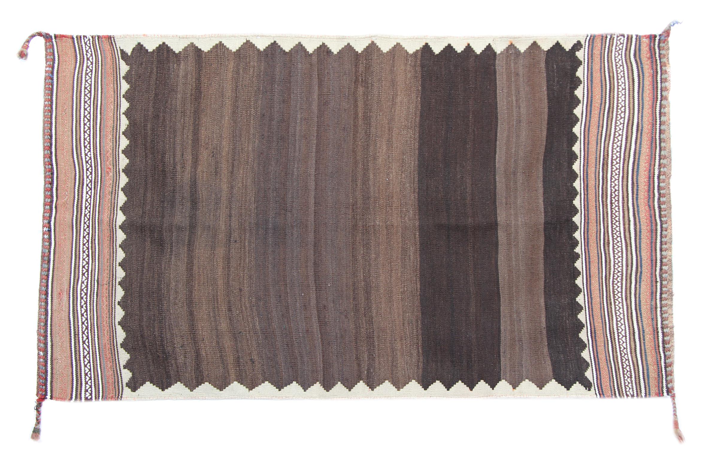 Dieser antike Sofreh-Kilim-Teppich aus den 1930er Jahren ist ein wunderschön erhaltenes Beispiel für handgefertigte Stammeskunst, gewebt aus ungefärbter Naturwolle in satten erdigen Brauntönen. Sein minimalistisches und dennoch auffälliges Design