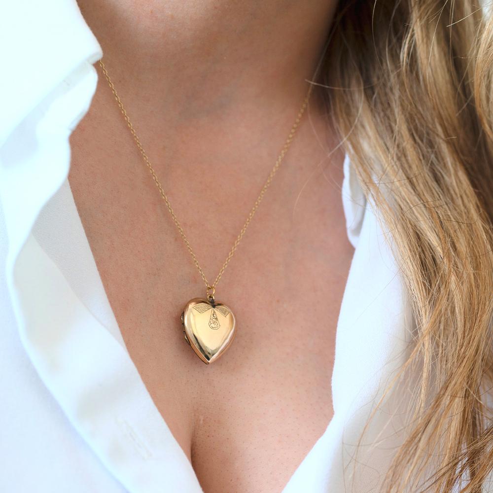 This charming antique heart locket necklace is crafted in 9ct yellow gold and features a beautifully engraved bow motif on the front—a sweet and symbolic detail often associated with love, memory, and affection. The reverse is polished and stamped