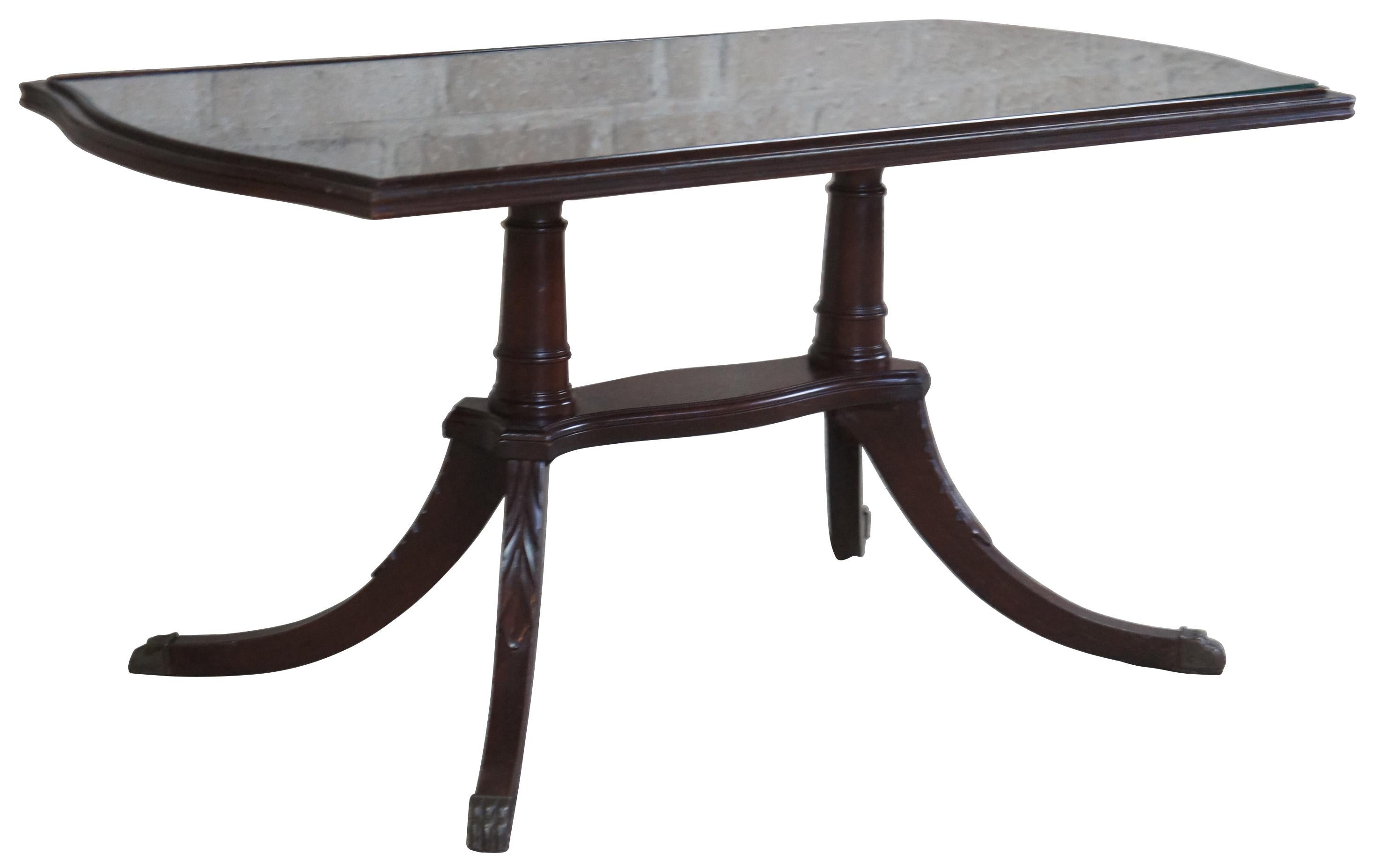 Circa 1940s Duncan Phyfe coffee or tea table. Made from mahogany with a rectangular form. Features a glass inset top supported by two pedestals leading to four flared legs capped with brass paw feet.
 